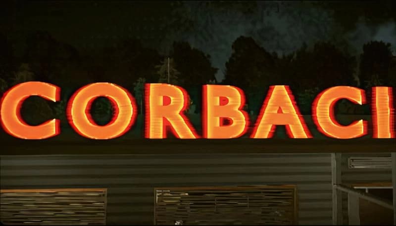 Corbaci: Large illuminated orange letters spell "CORBACI" atop a dark building against a forest backdrop under a night sky.