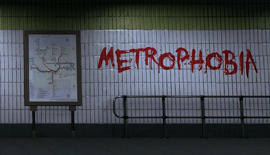 Metrophobia: graffiti-style red title painted on white tiled metro wall beside framed subway map and railings.