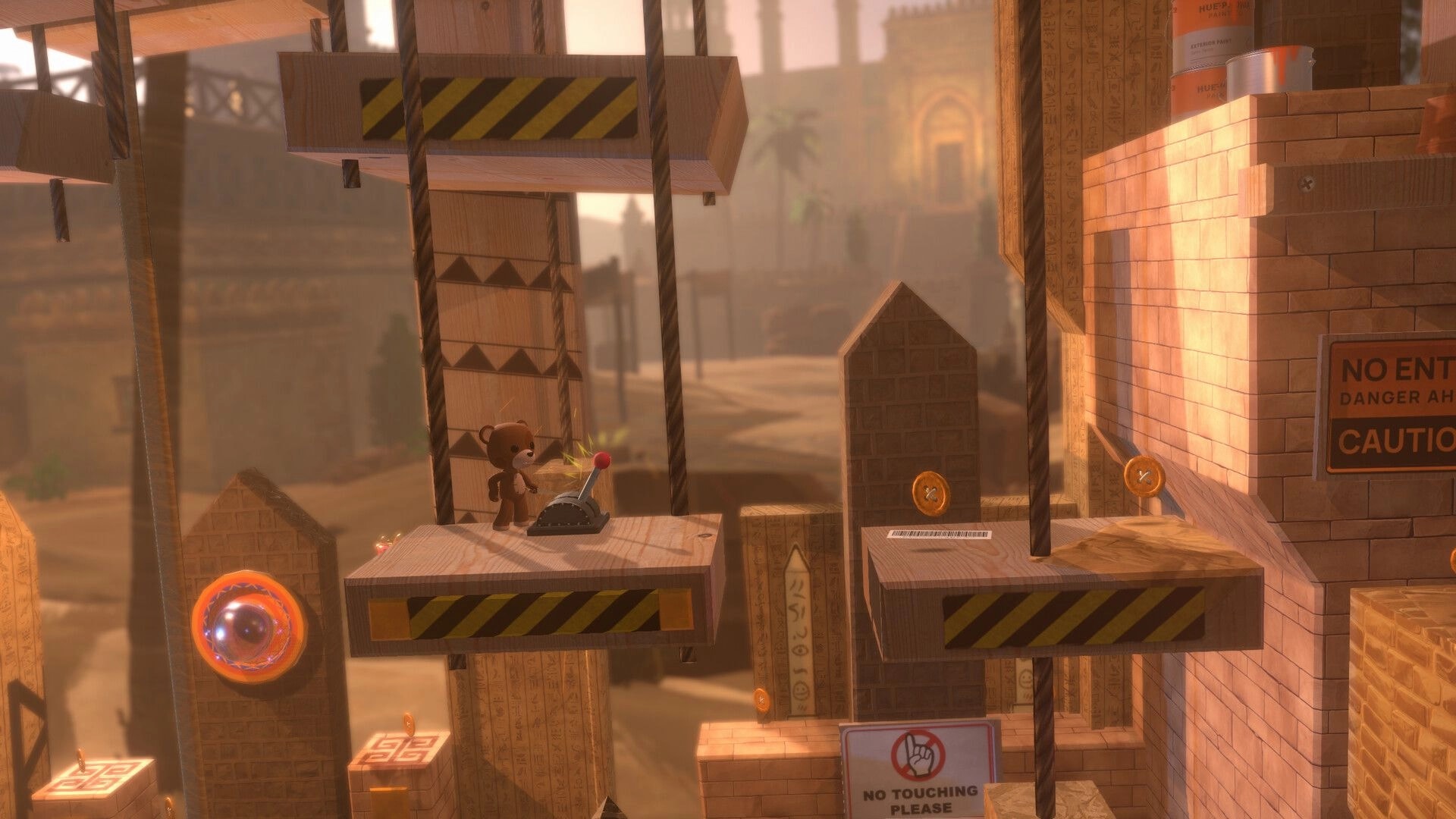 Restitched: Teddy character pulls a lever on a hanging platform in a dusty brick ruin with coins nearby.