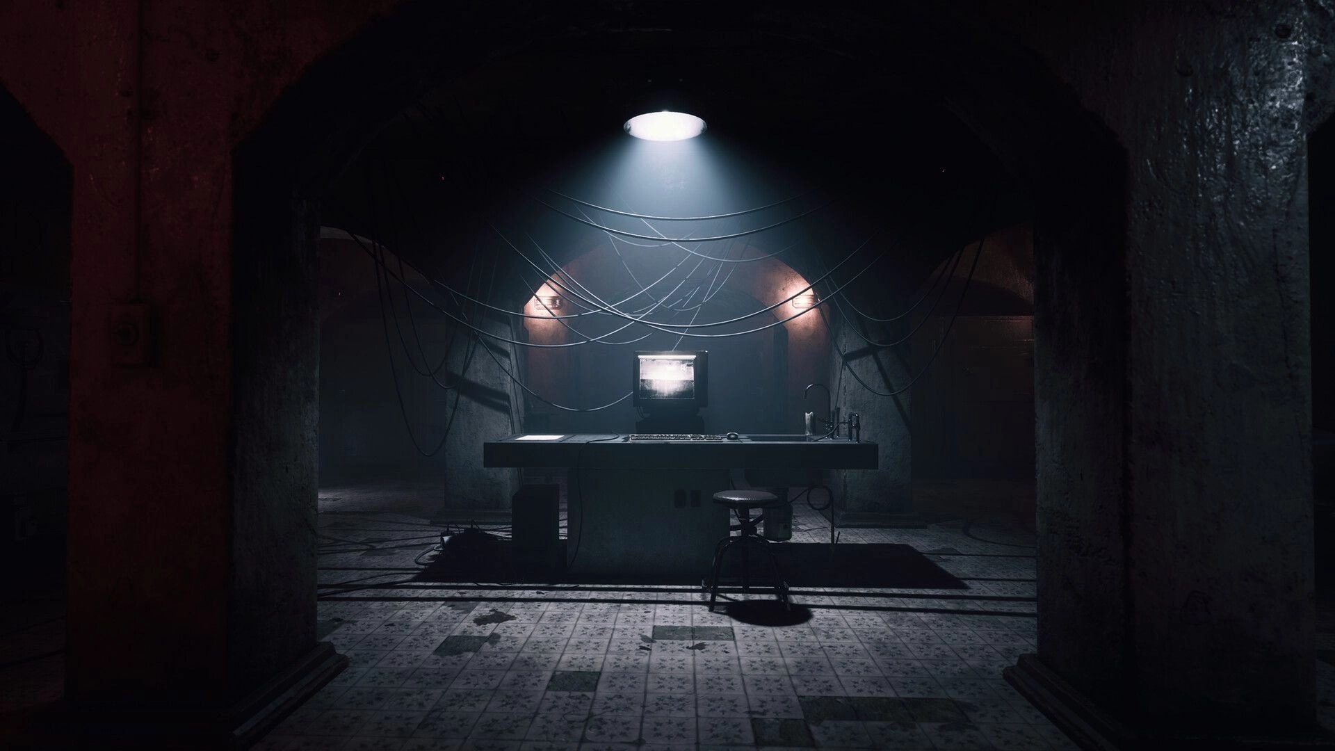 UNHOST: Surveillance monitor on a desk under hanging cables in a dim, tiled underground room.