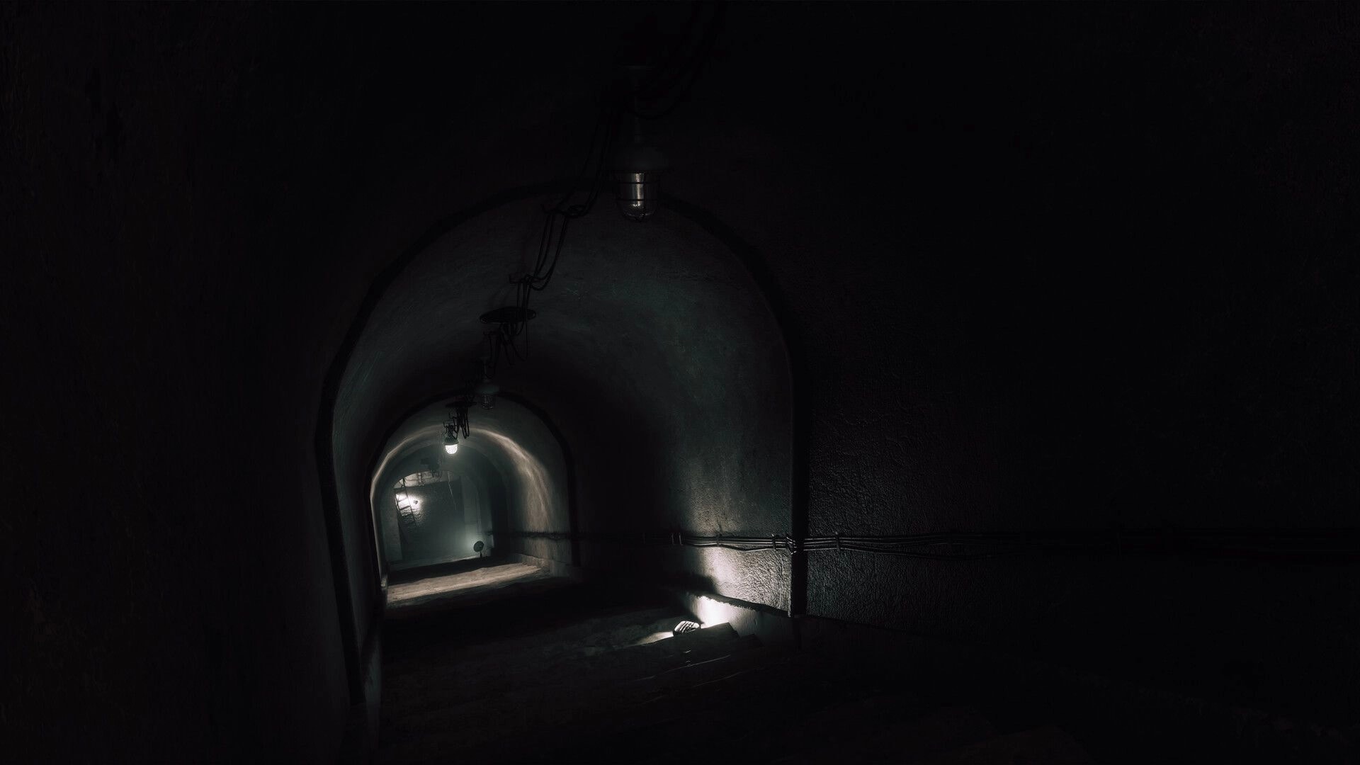 UNHOST: Dim stairwell descending into an arched corridor lit by a single bulb in shadowy tunnels.