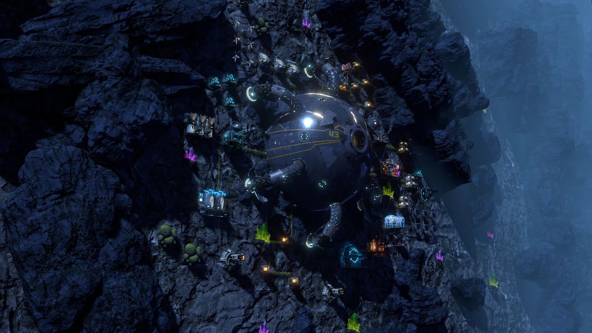 Wall World Strategy: Robo-spider base with mining rigs and lights clinging to a steep rocky wall cavern.