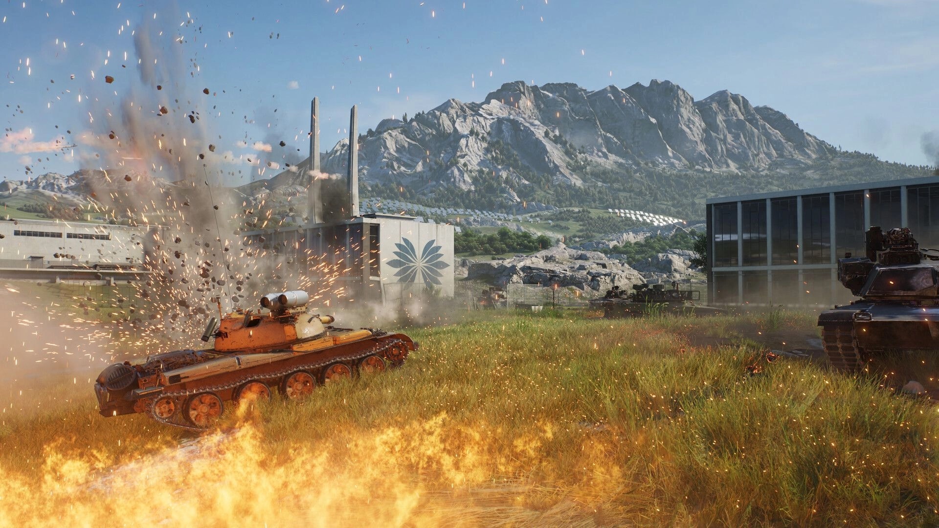 World of Tanks: Tank hit by explosion near factory buildings and mountains, flames in grassy field.