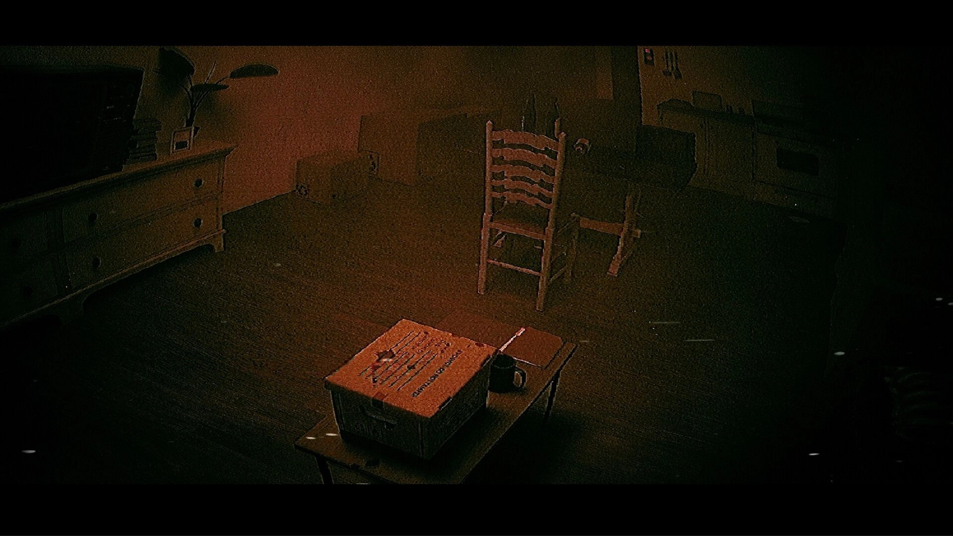 ALONE: Grainy view of a box and mug on a table in a dim room with chairs and cabinets.