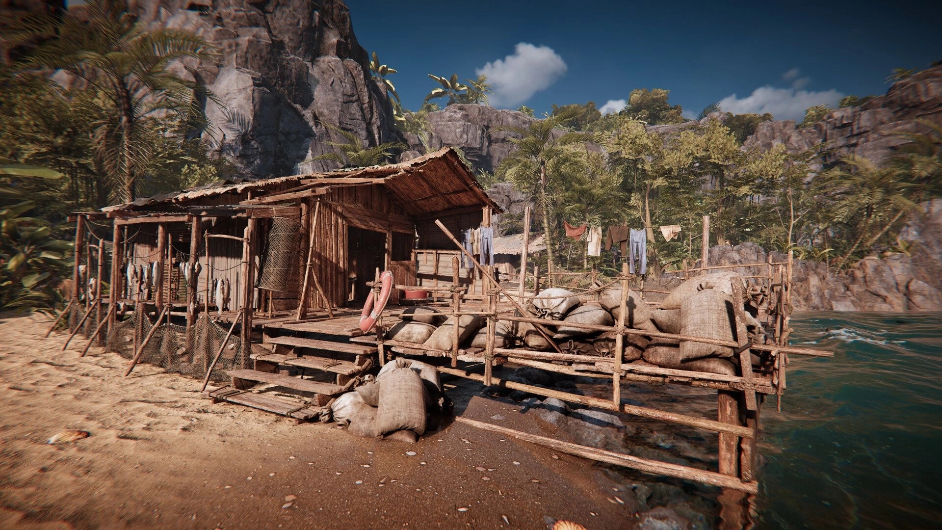 Amerzone: Wooden shack with fishing nets and sacks on a sandy beach by a lush jungle and rocky cliffs