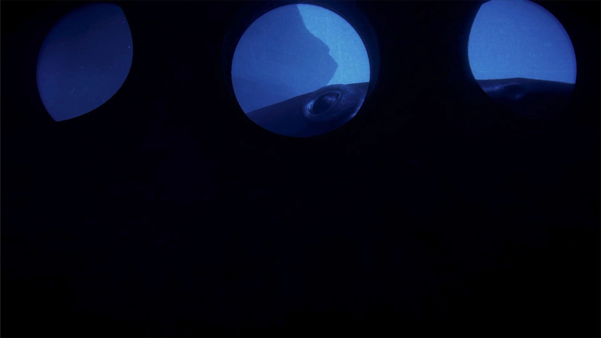 BATHYSPHERE: Three round porthole windows view dark blue ocean and the sub hull in shadowed cabin.