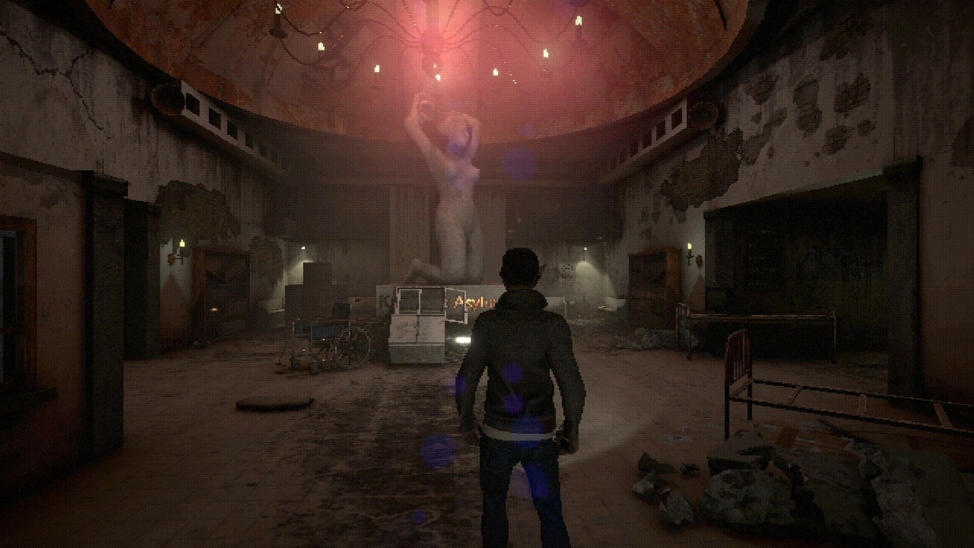BECROWNED: Player explores decrepit hall with a large statue under red light in an abandoned asylum.