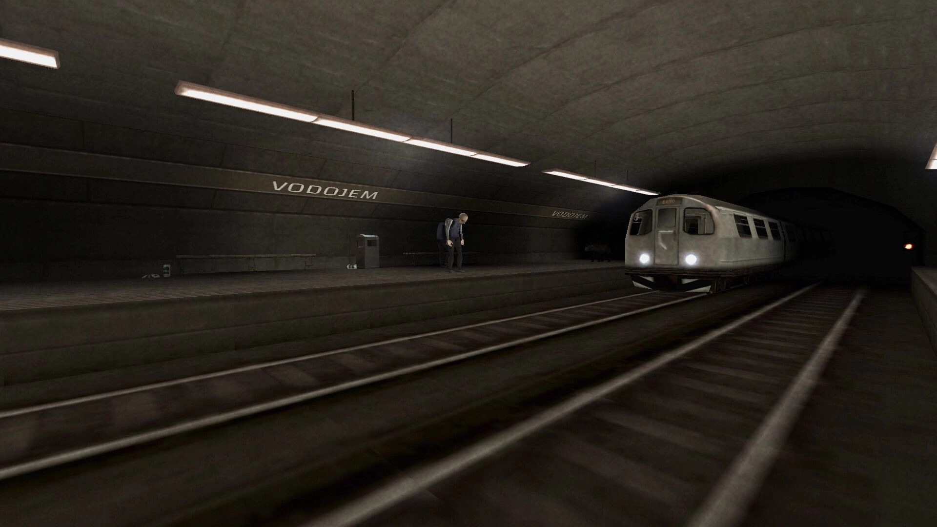 Brno Transit: Metro train arriving at dimly lit Vodojem station with two figures on the platform