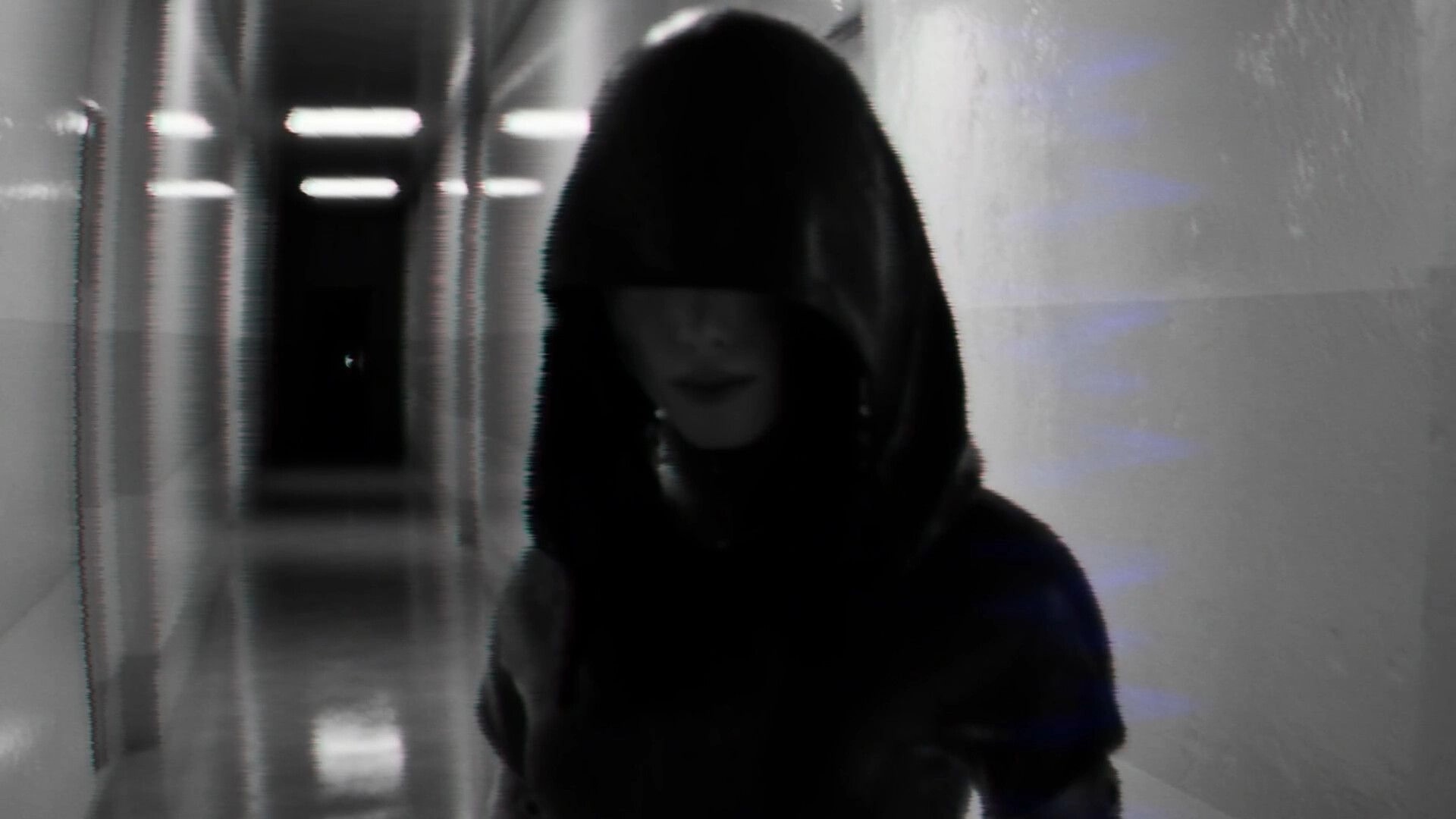 BrokenLore: Hooded figure with face obscured stands in a blurry, fluorescent-lit hospital corridor.