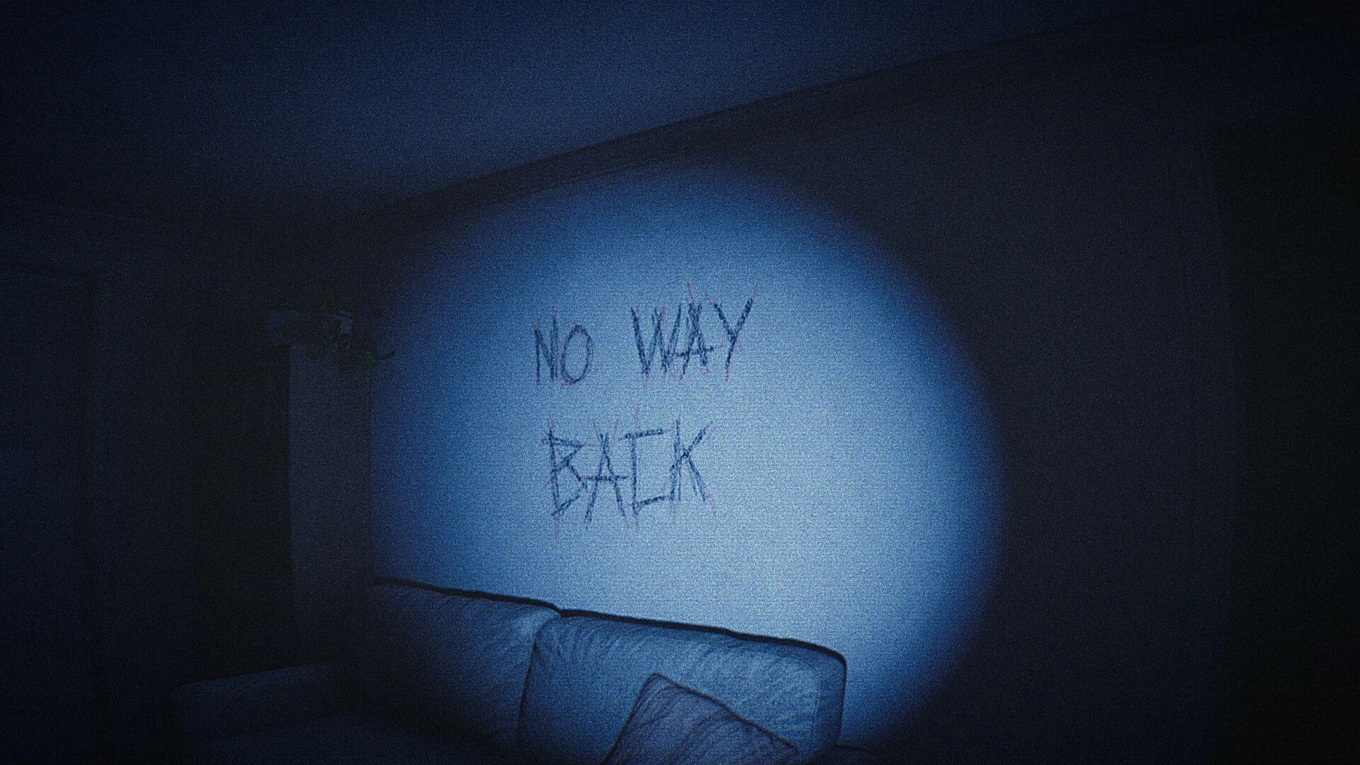 CAPTURED 2: Flashlight highlights “NO WAY BACK” scratched on wall above couch in dark room.