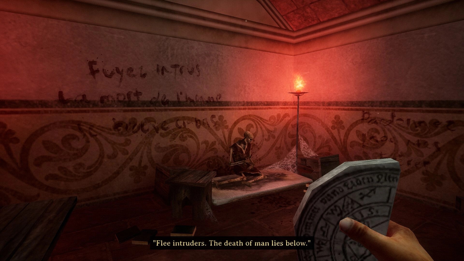 Caput Mortum: Player holds a cryptic stone in torchlit room with eerie writing and skeletal remains.