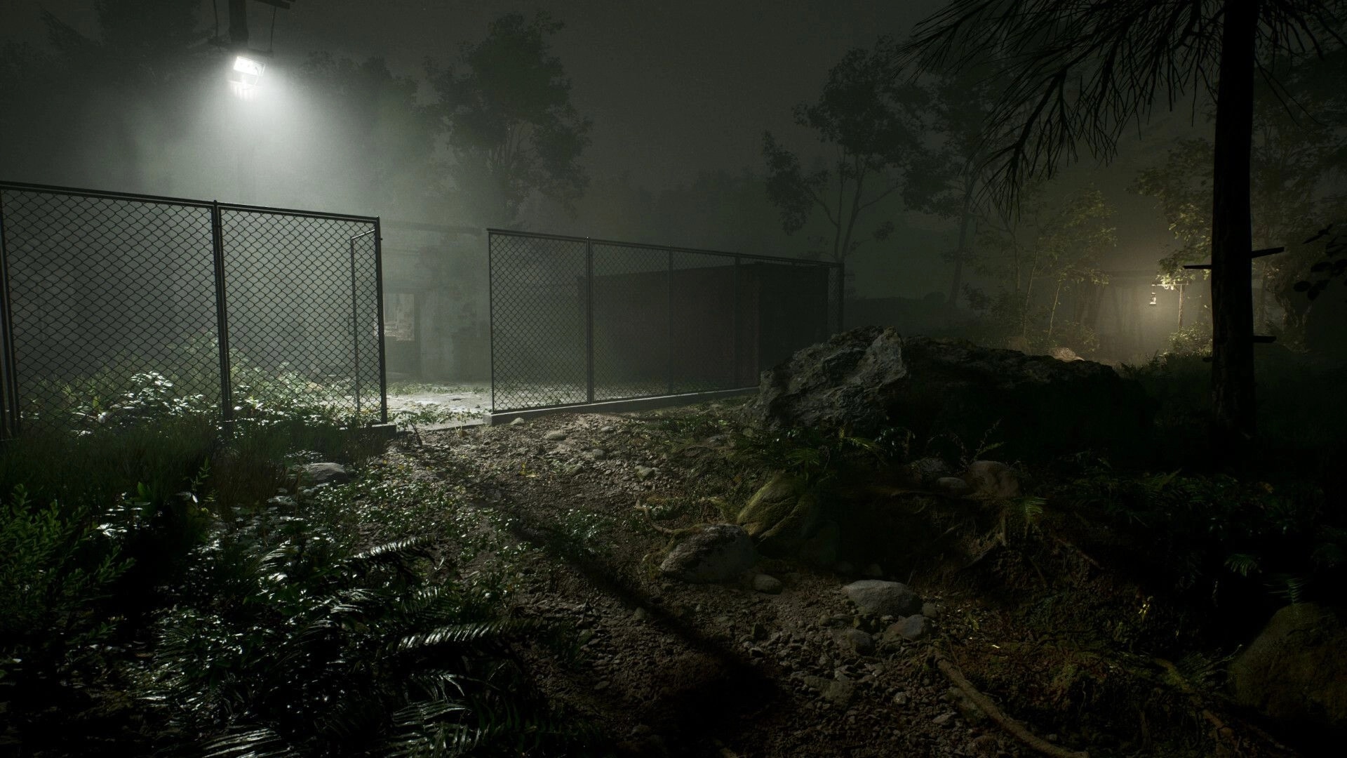 Cosmic Fear: Foggy forest path by chain-link fence under harsh floodlight near a shadowy building.