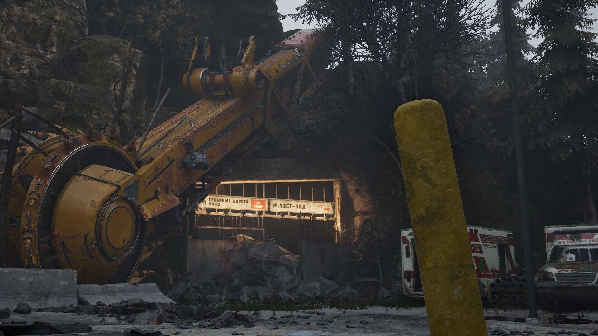 Desserted: Entrance to a cave with a large yellow drill surrounded by emergency vehicles in a forest.