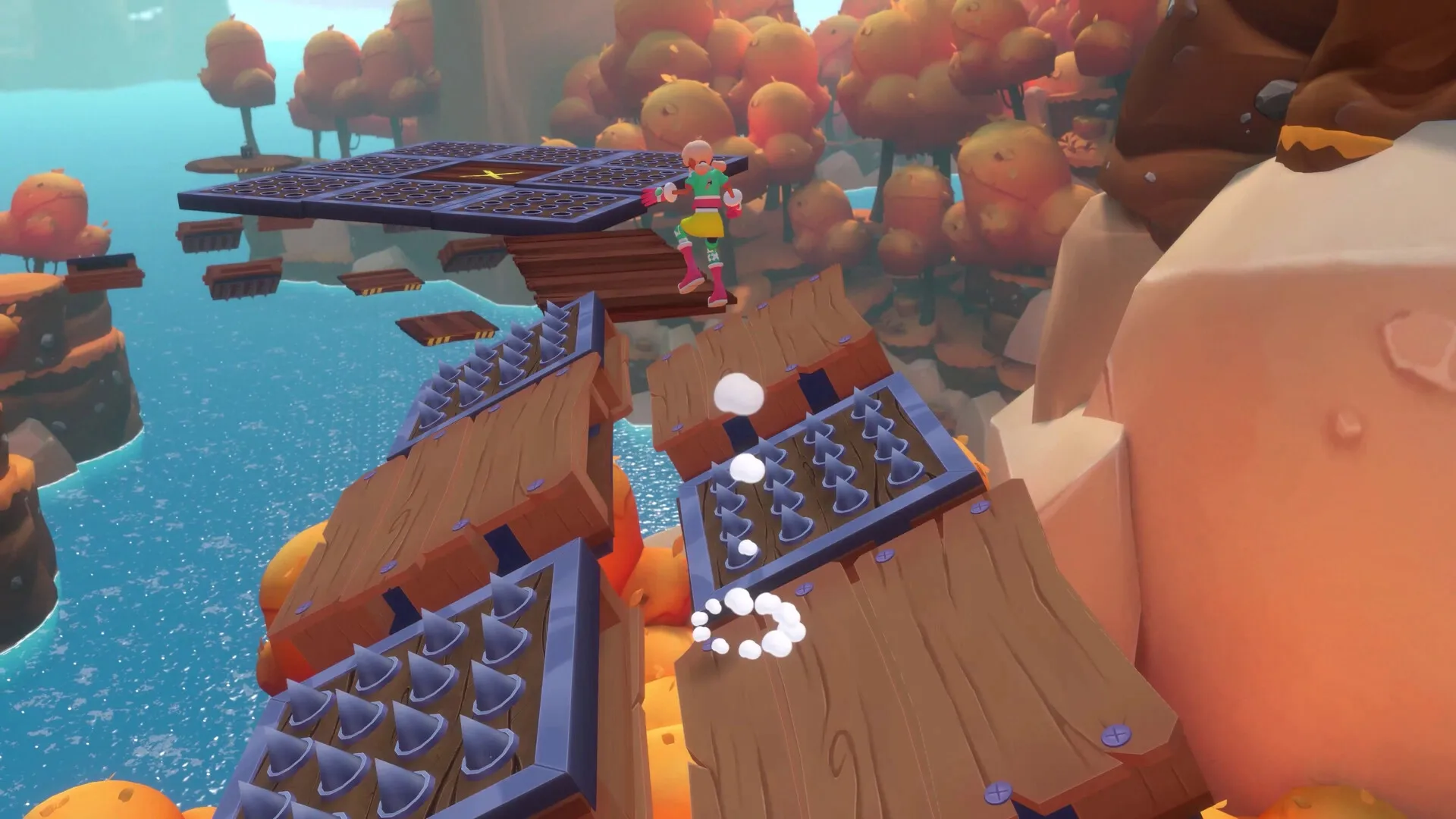Dracamar: Caliu jumps over spiked platforms in a colorful forest with floating wooden bridges nearby