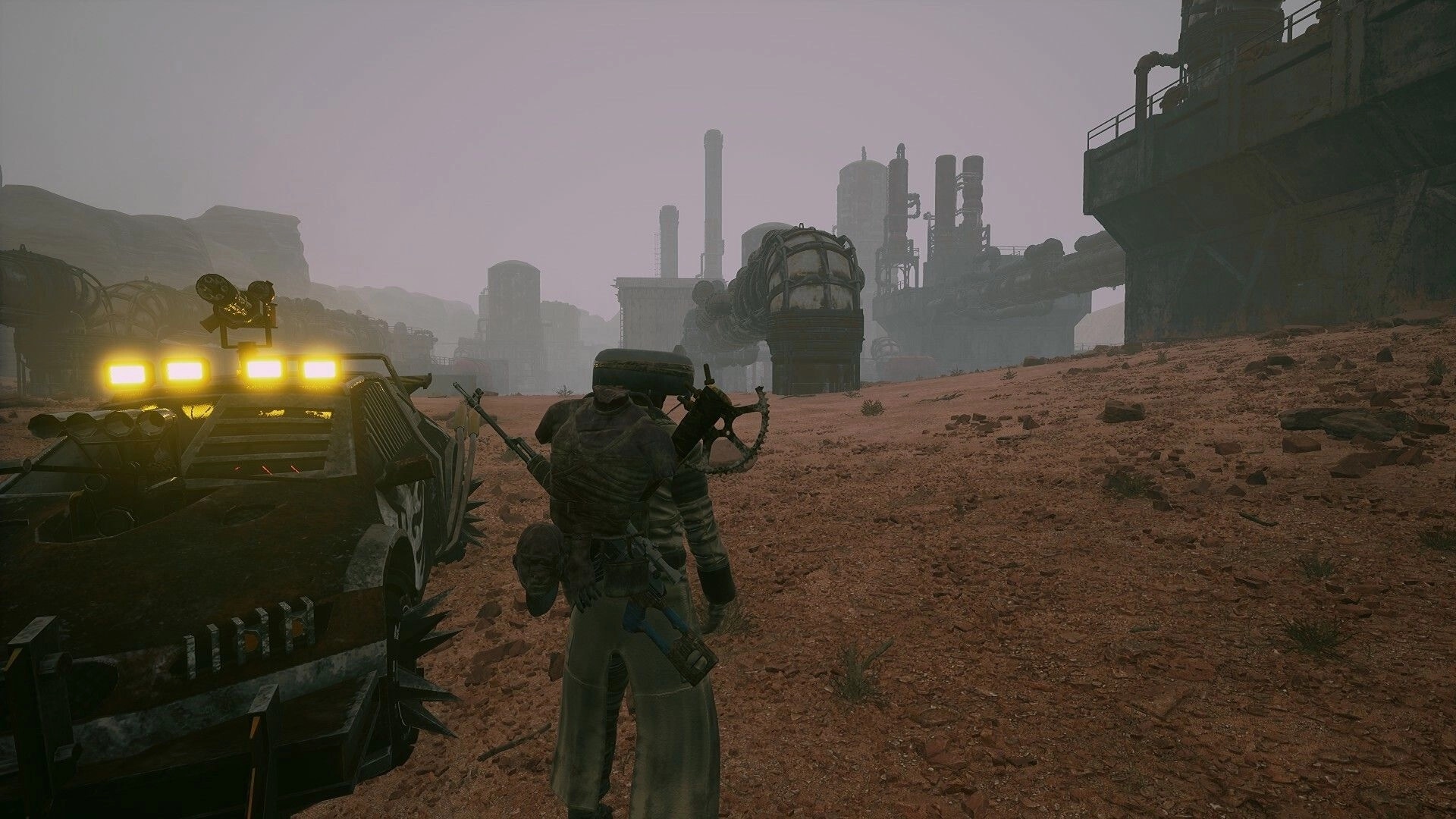 Duneborn: Player stands beside armored vehicle in industrial desert landscape with factories ahead.