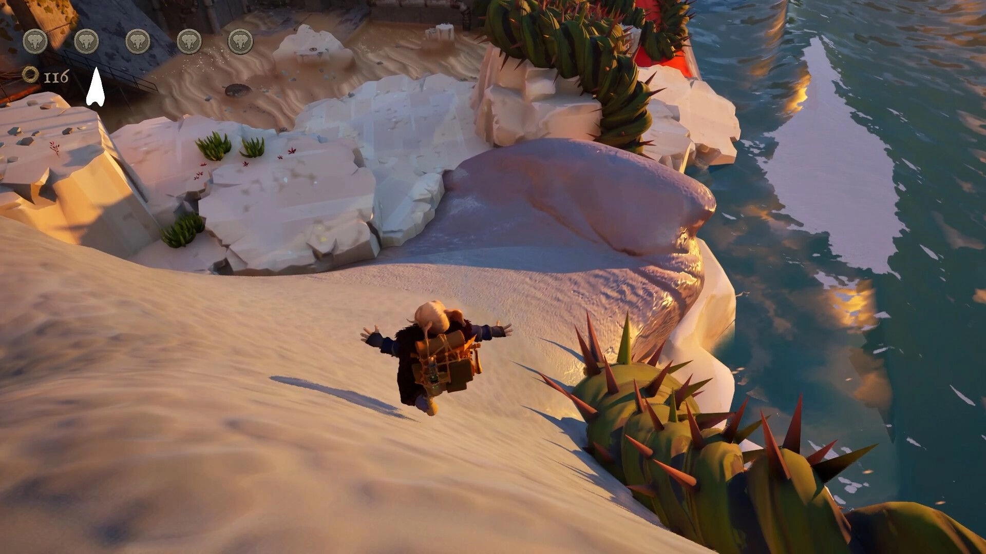 Enfant: Elephant protagonist descends a sandy slope near a cliff with water and cactus-like plants nearby.