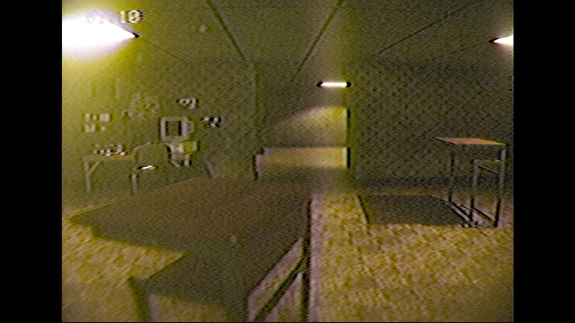ENTRY_13: Grainy VHS-view exploration past a metal cart and bench in a dim, tiled corridor room.