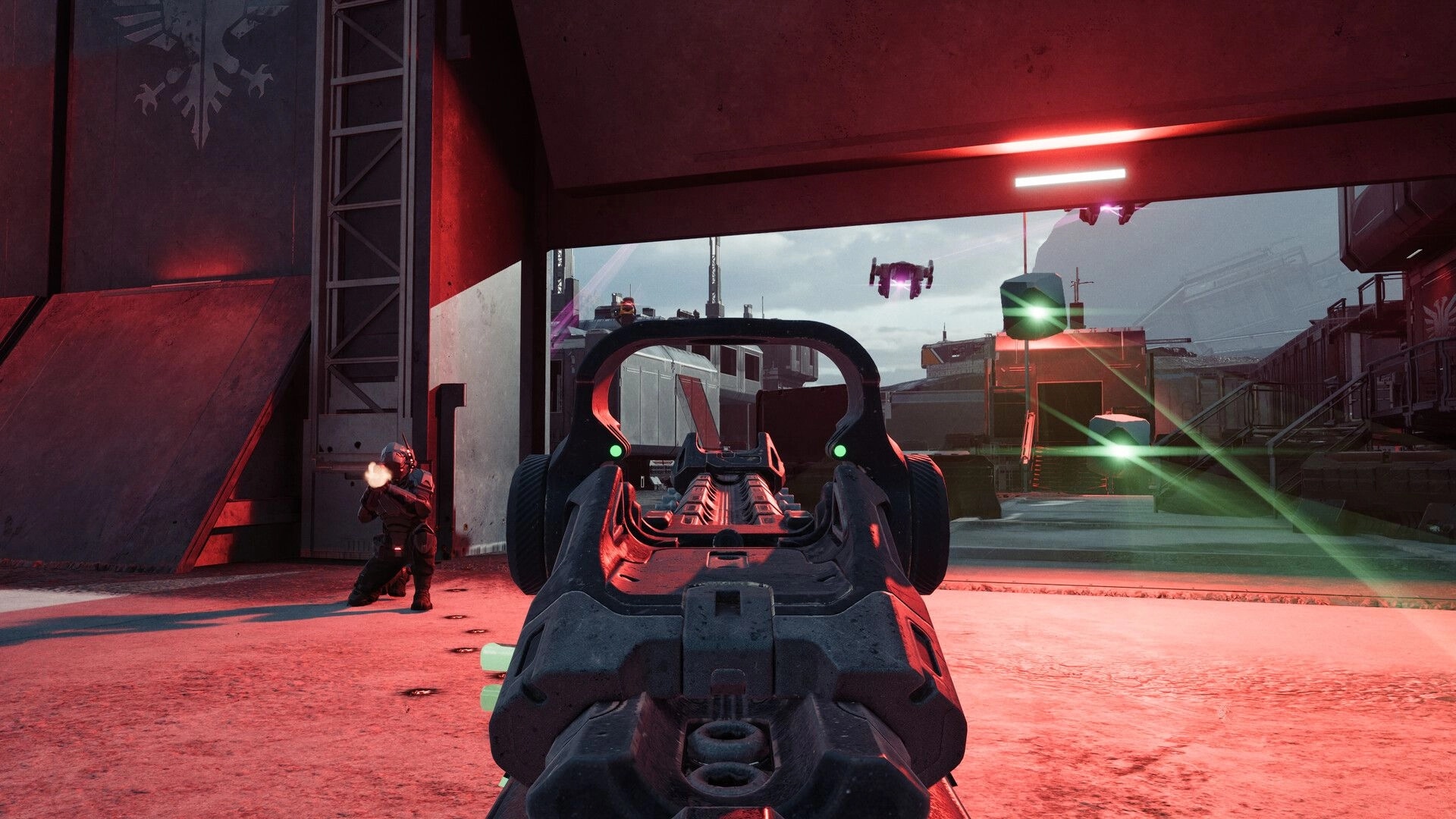 EVE Vanguard: Aiming down rifle sights at a drone while a teammate fires in a red-lit base yard.