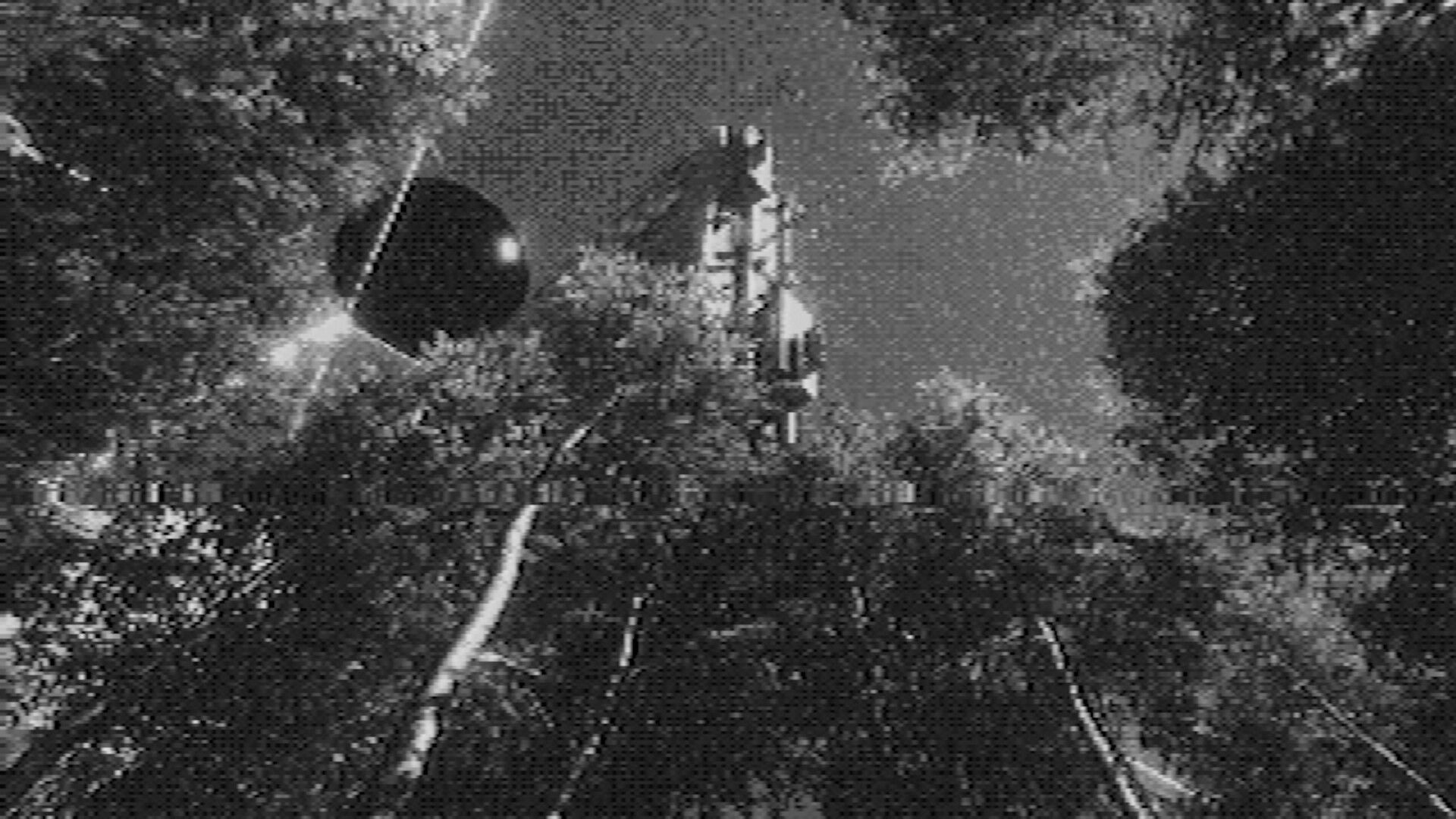 Fallgrade: Grainy first-person view of a hovering orb and tall tower amid dense foliage at night.