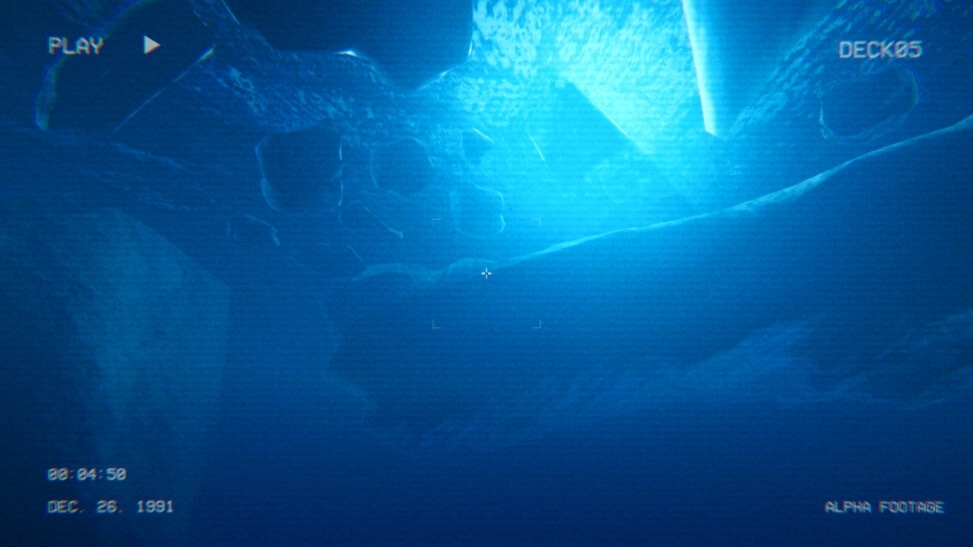 Full Fathom: Grainy deck camera view of dark seafloor rocks with HUD timecode and PLAY overlay.