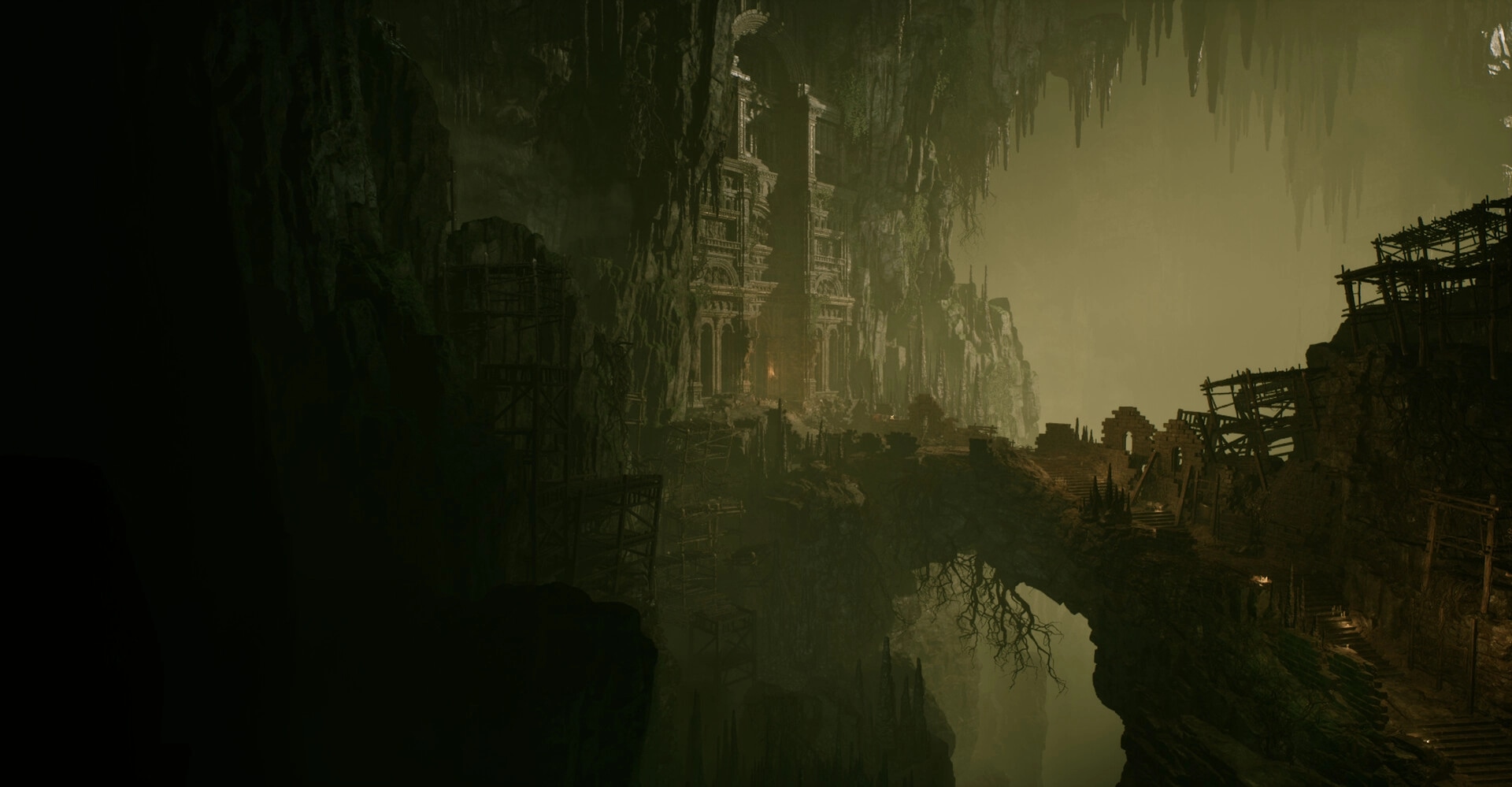Godless Dawn: Wide view of a ruined cliffside fortress and scaffolds inside a misty cavern abyss.
