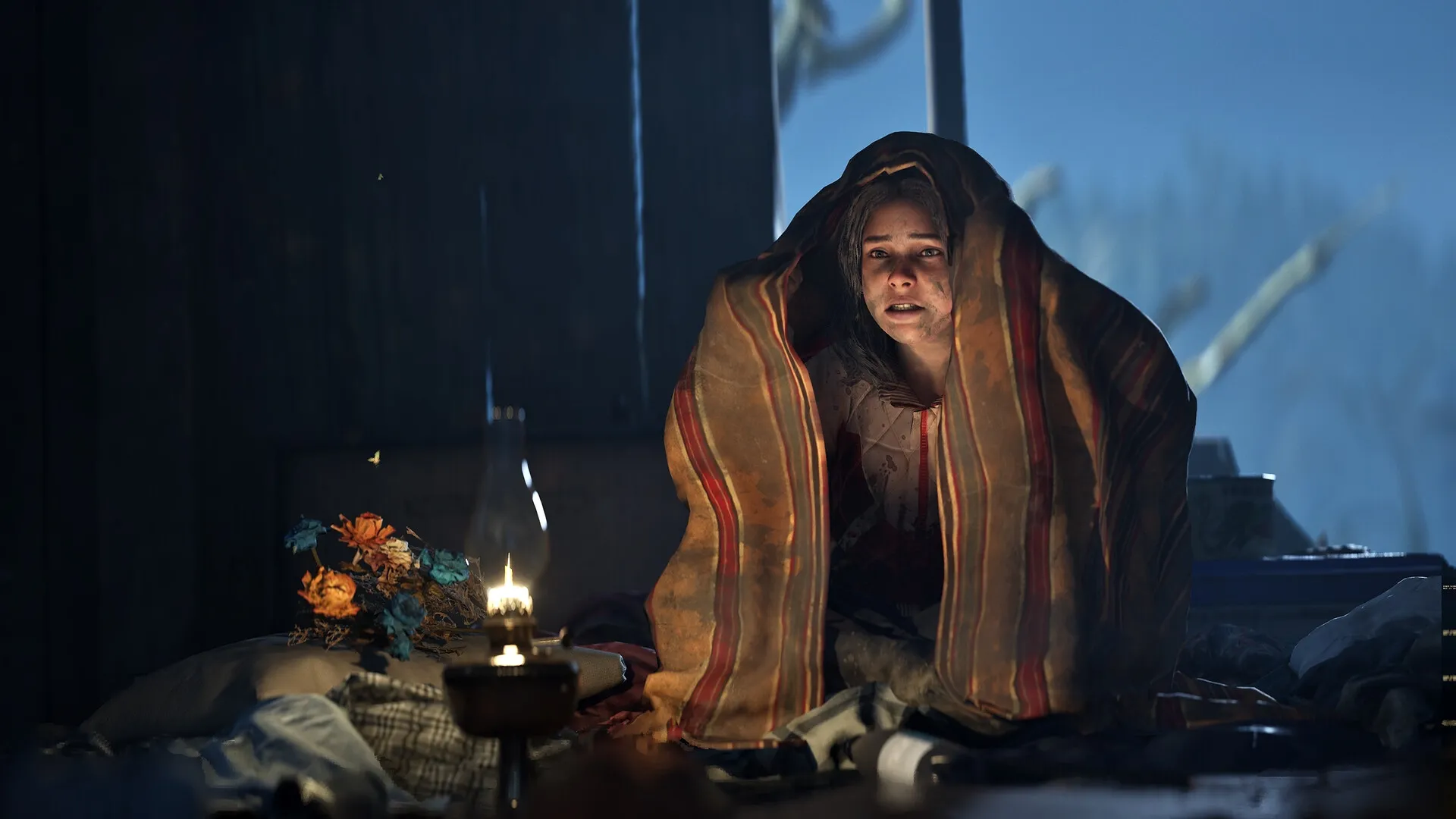 Hell is Us: Woman under a blanket with a lantern in a dimly lit room, surrounded by scattered objects.