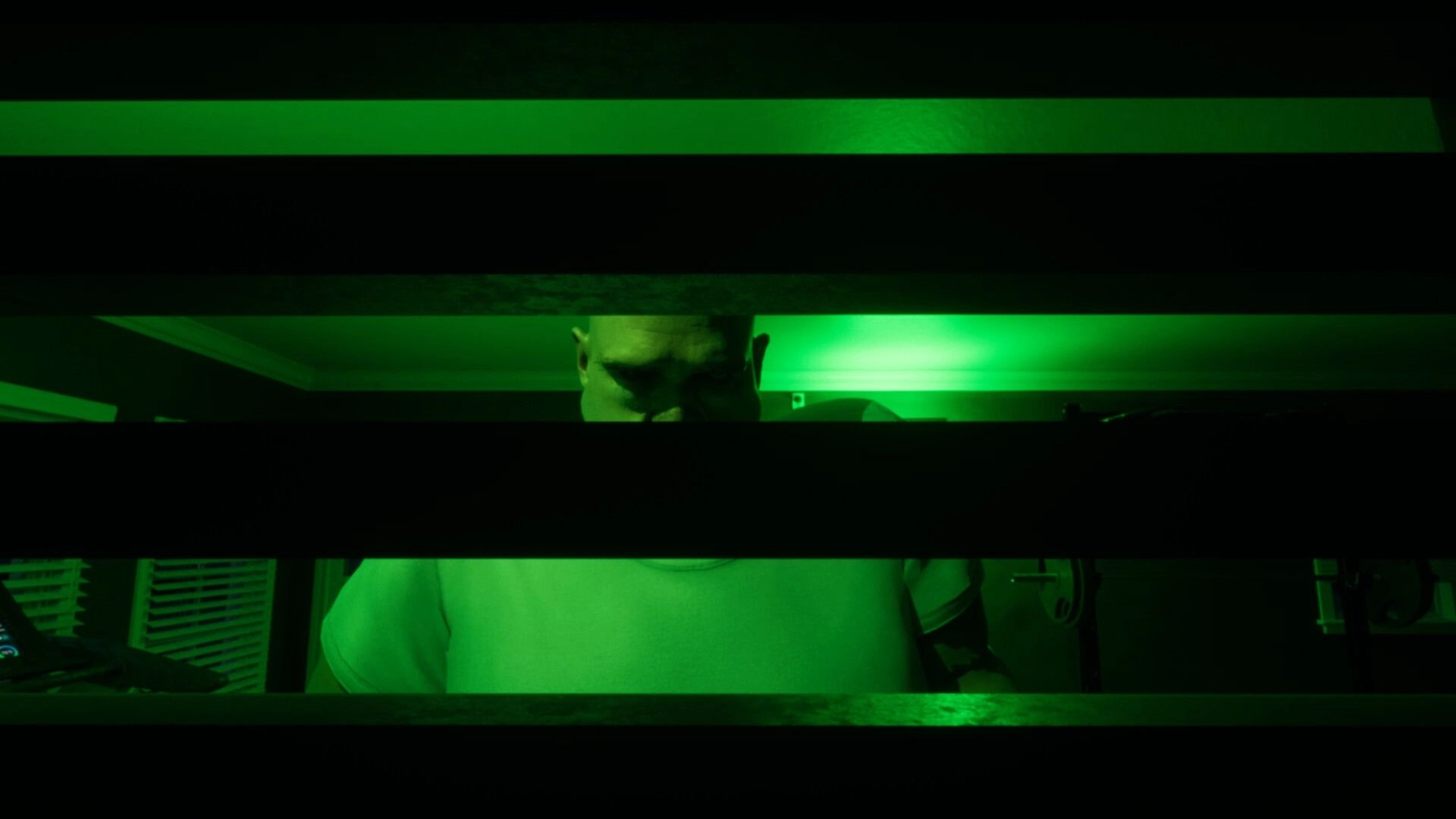 LAG KILLS: Man in white shirt seen through slats under green night vision inside a house room.