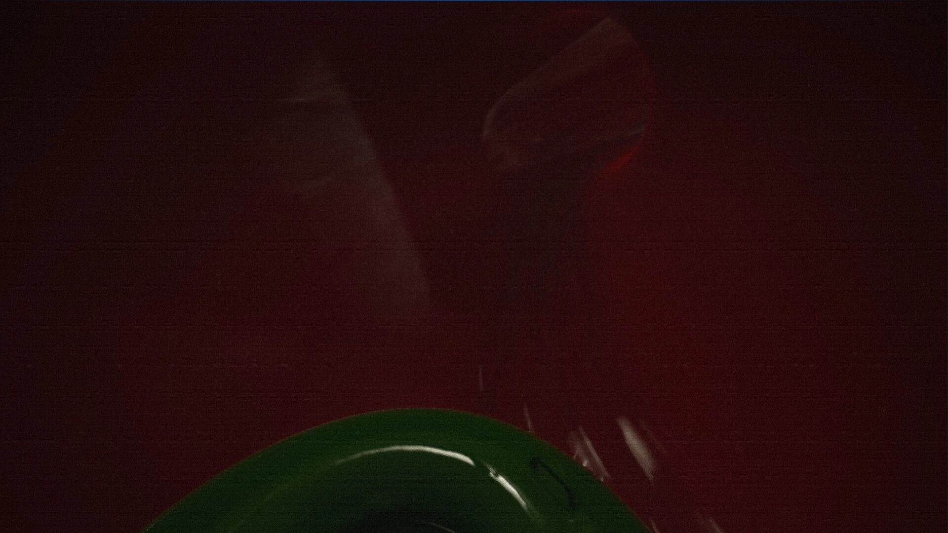 Late Shift: Close-up of a green hard hat at bottom of frame against a dark red blurred wall.