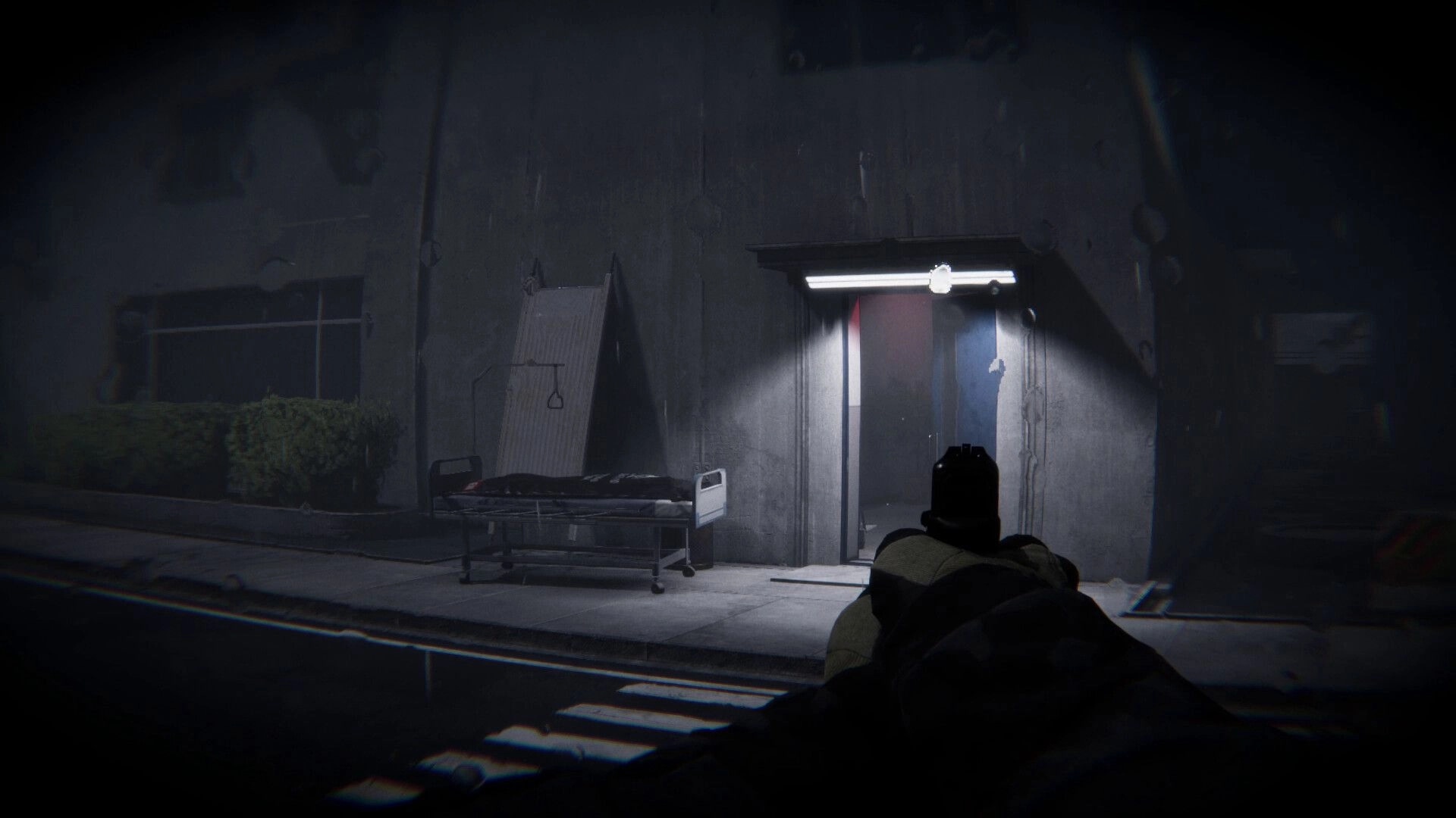Lens Of Fear: First-person view aiming at a lit doorway beside a gurney in a dark hospital corridor.