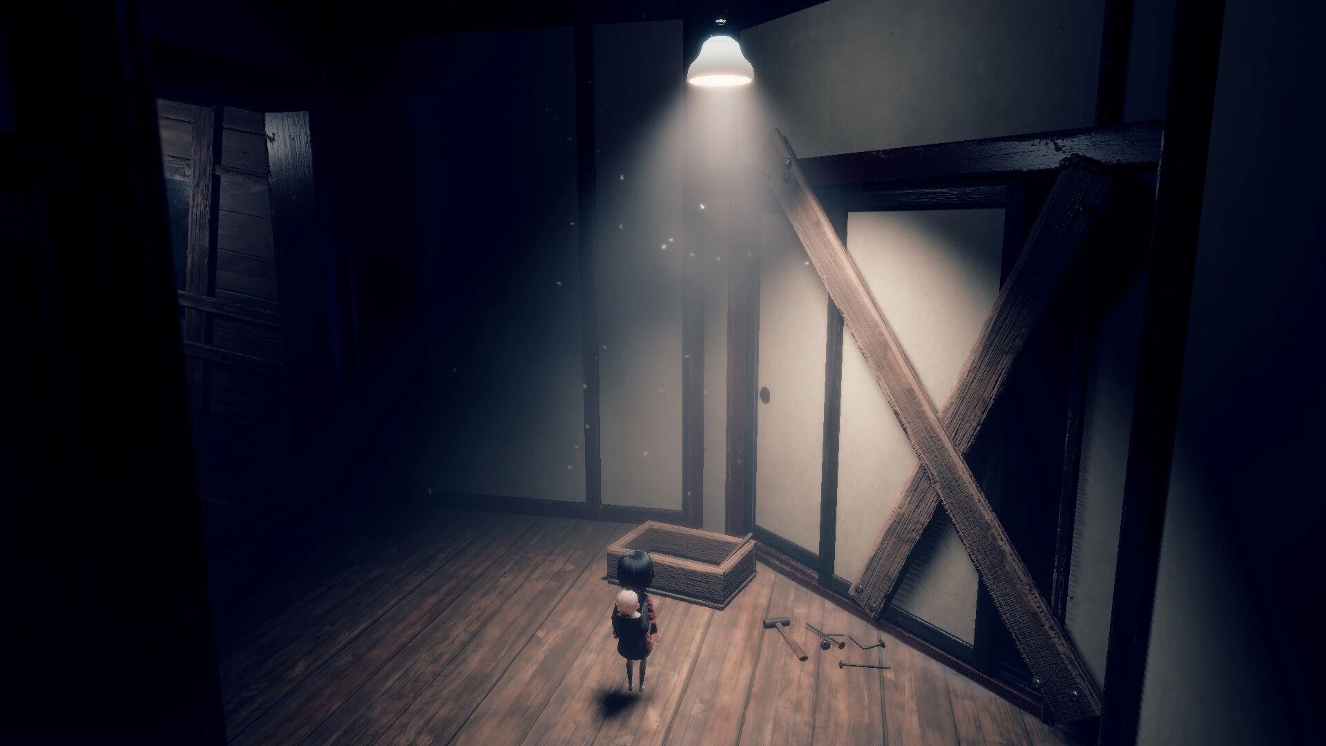 Lull: Girl with baby on back stands by a boarded door and scattered tools in dim wooden room.