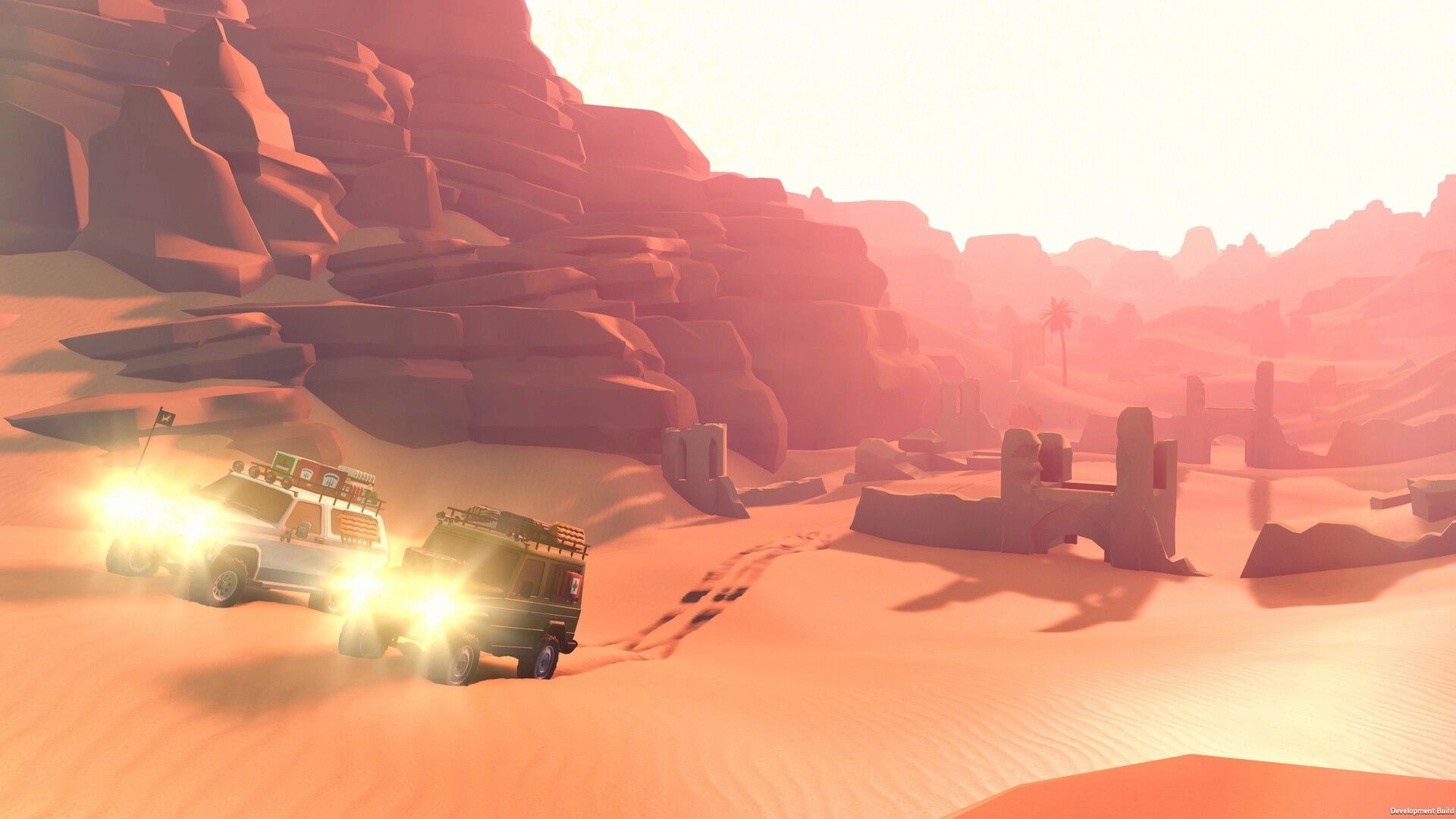 over the hill: Two off-road trucks with headlights on drive through desert dunes beside rocky cliffs at sunset.
