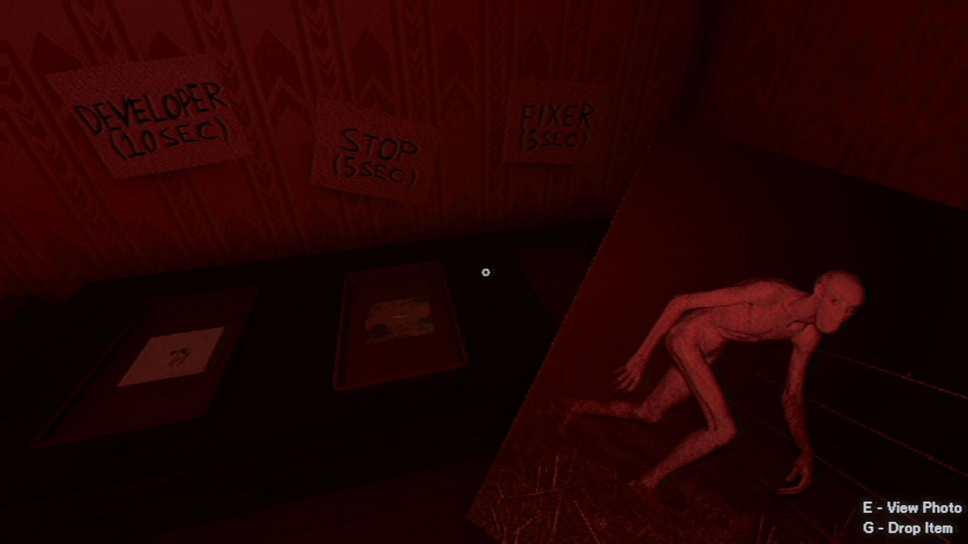 Photomaly: Darkroom timer buttons on wall beside a crawling humanoid figure in red-lit room.