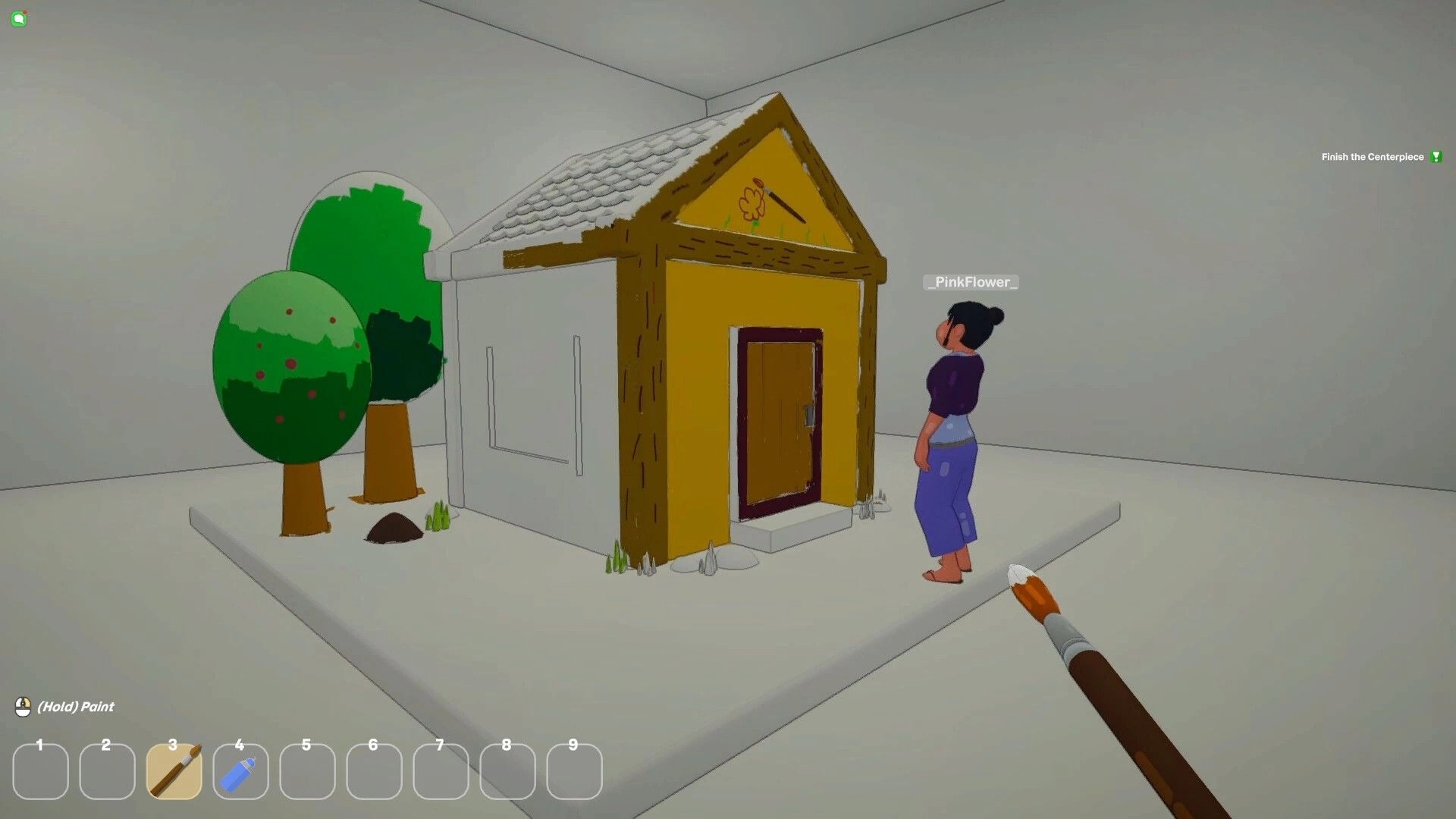 Picasho: Player holds paintbrush facing small house diorama with trees and PinkFlower in studio room.
