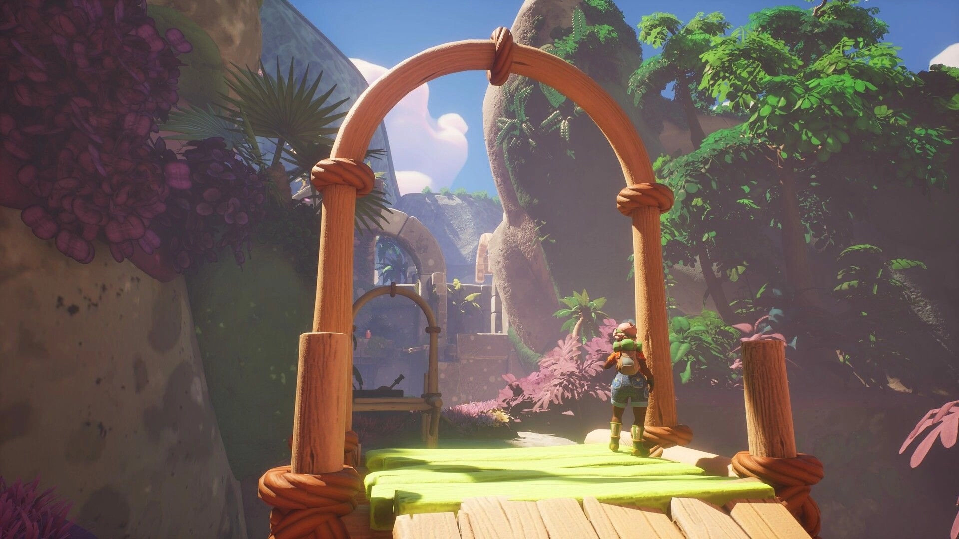 Portabellows: Player character on a wooden bridge under an arch in a lush canyon with ruins ahead.