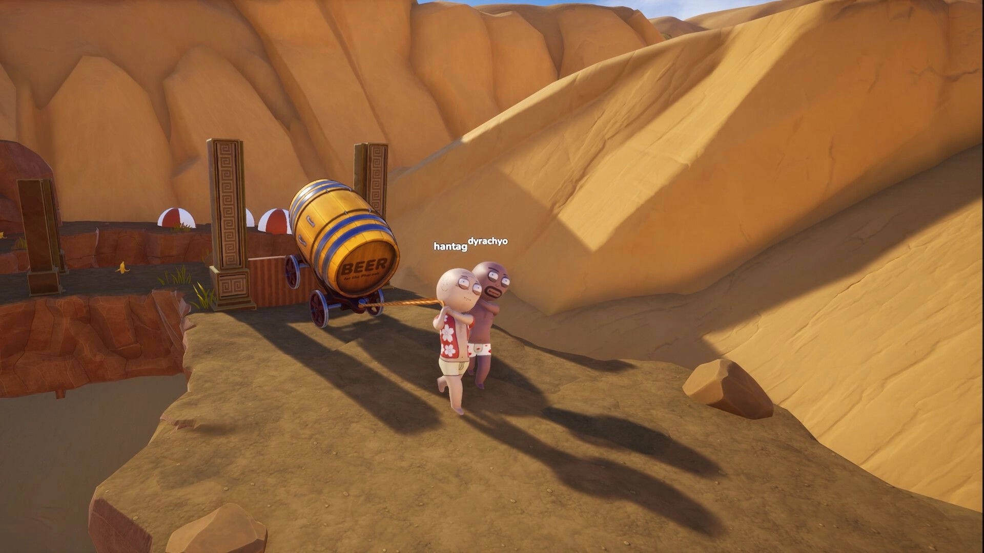 Pull the Beer: Two co-op players pull a beer barrel cart by rope along a sandy canyon ledge.
