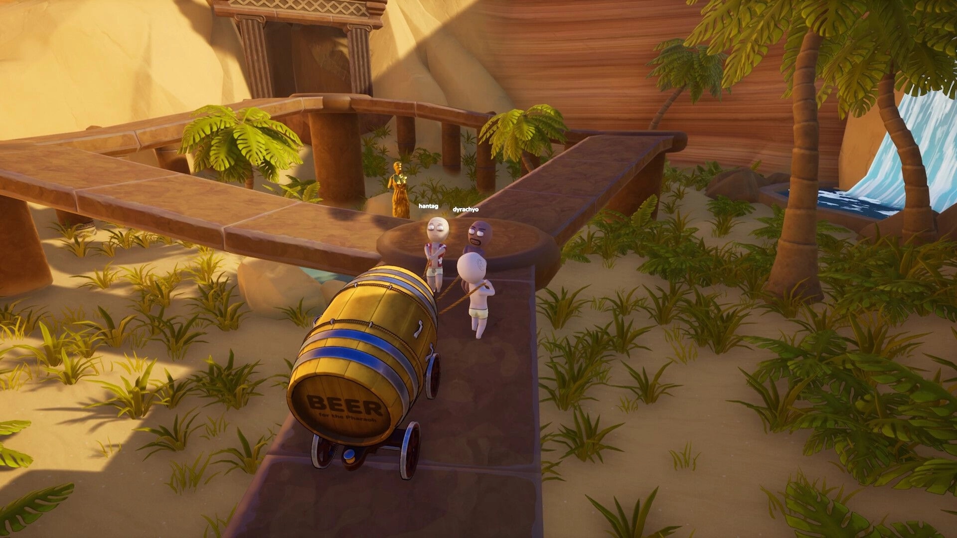 Pull the Beer: Two co-op avatars pull a wheeled beer barrel along temple ruins by a waterfall oasis.