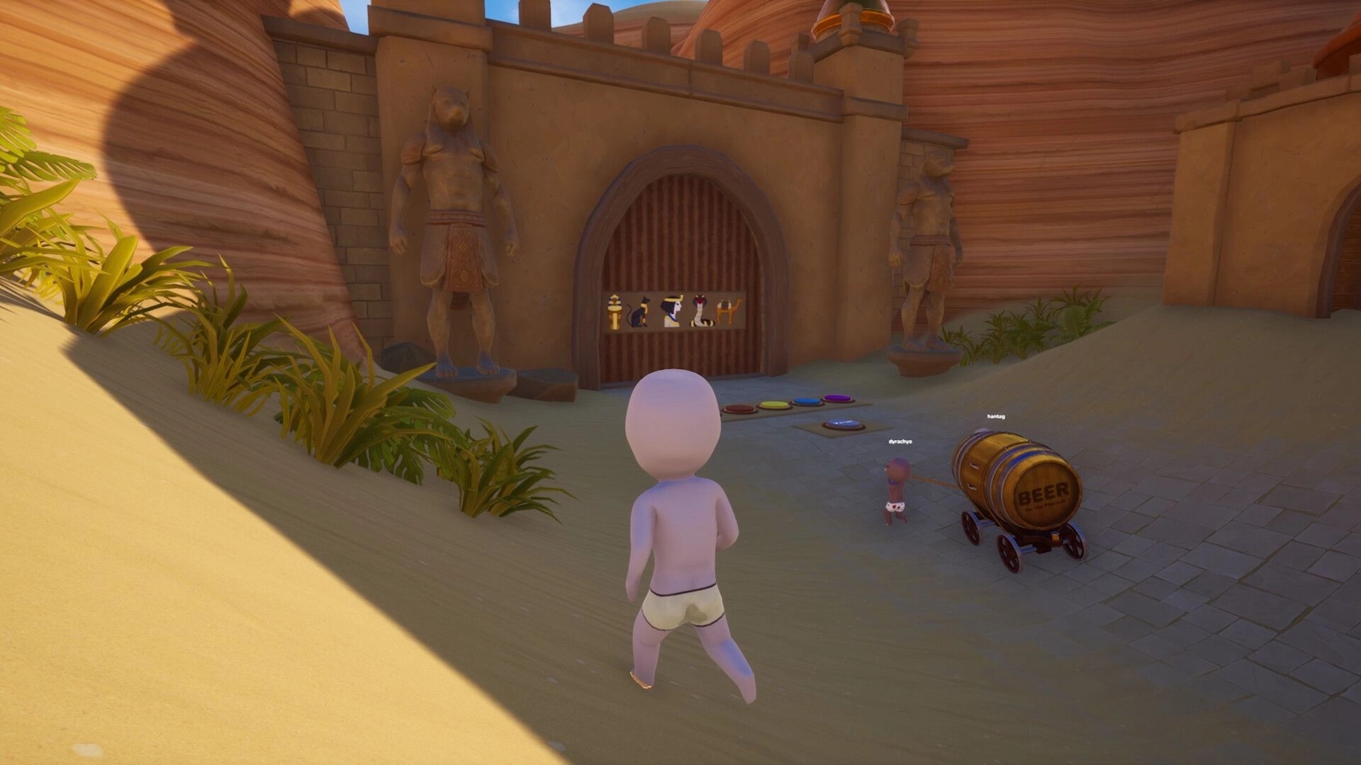Pull the Beer: Two co-op characters pull a beer barrel cart toward a temple gate in desert canyon ruins.