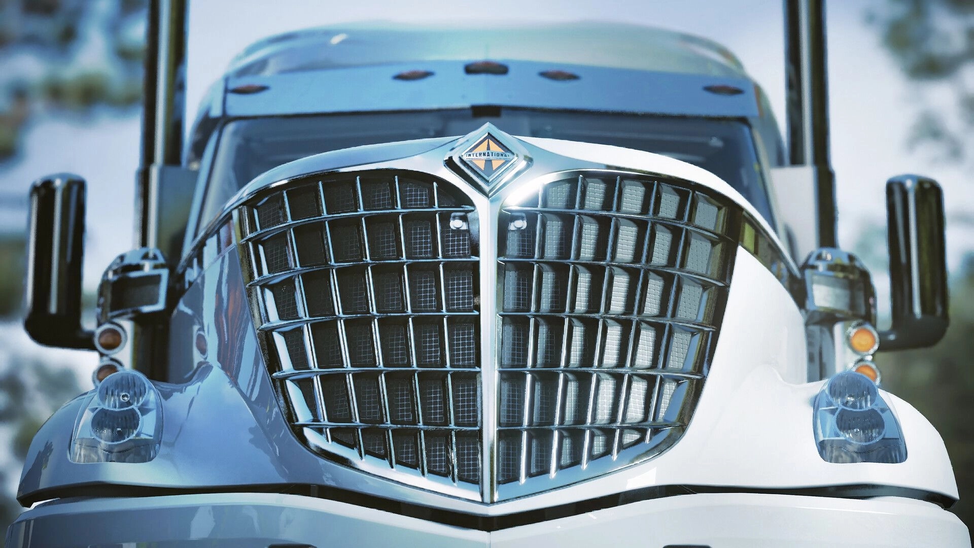 Road Kings: Close-up of a semi truck grille and headlights in bright daylight with blurred road behind.