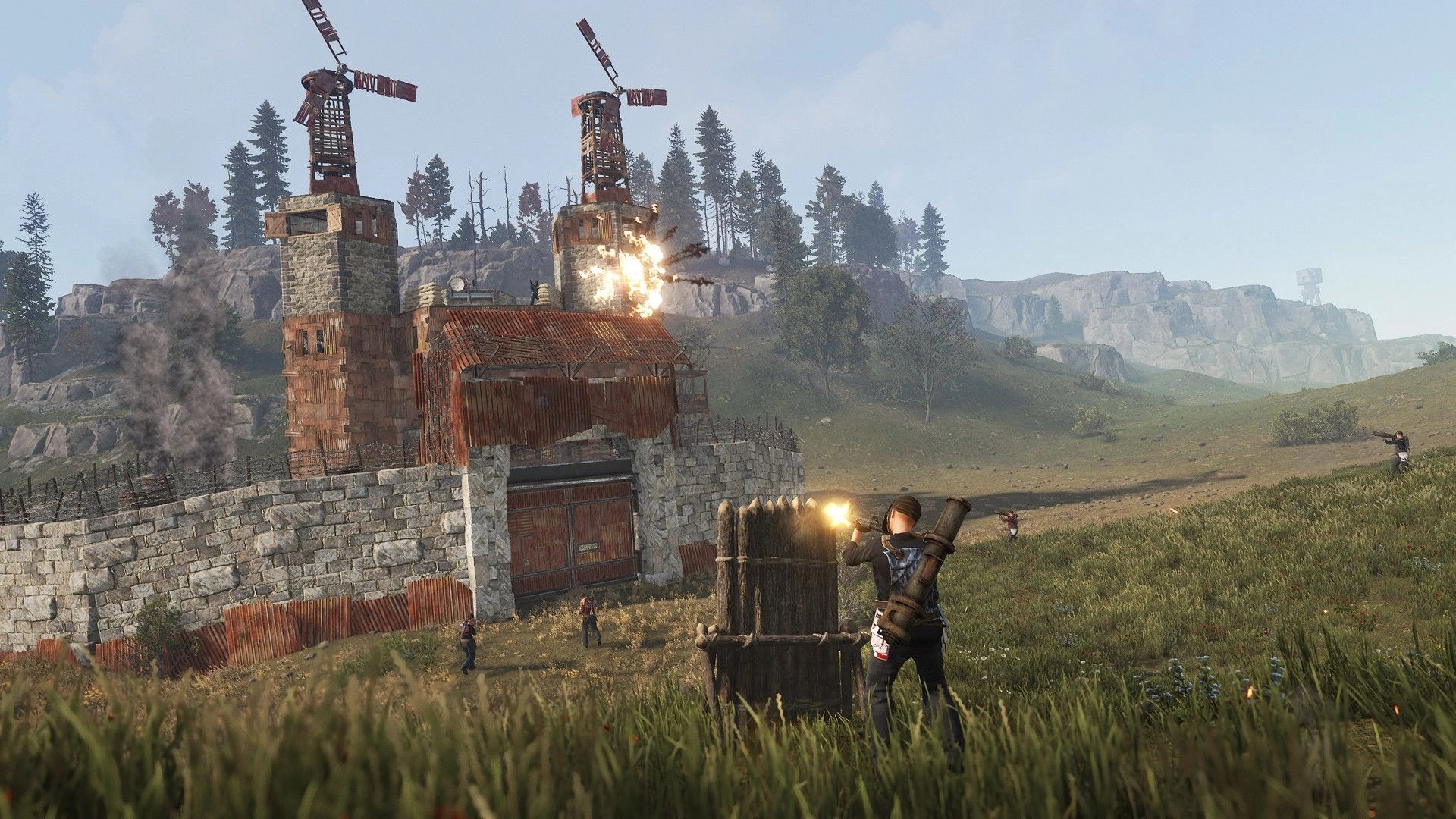 Rust: Players attack fortified base with explosions in grassy landscape with stone walls and windmills.