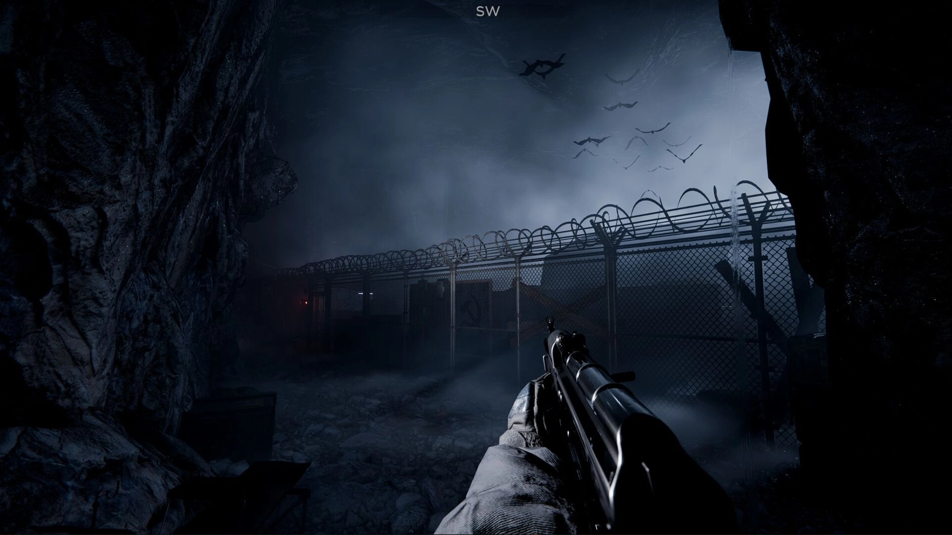 Shadow Project: First-person view aiming at a barbed wire fence in a dimly lit, rocky environment