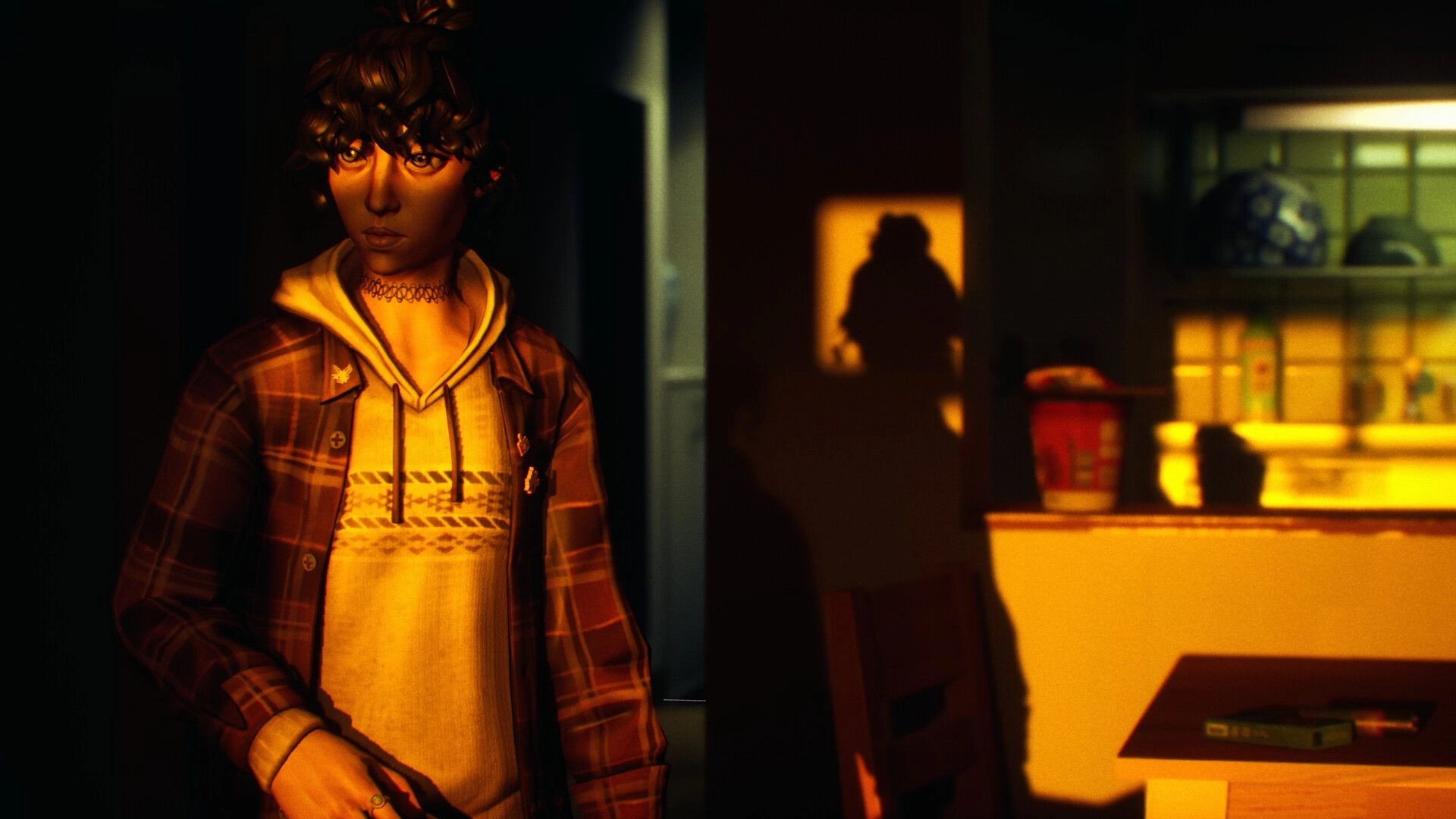 SOMBRAS: Close-up of Shiomi lit by warm light in a dim room, with a shadowy figure in doorway.