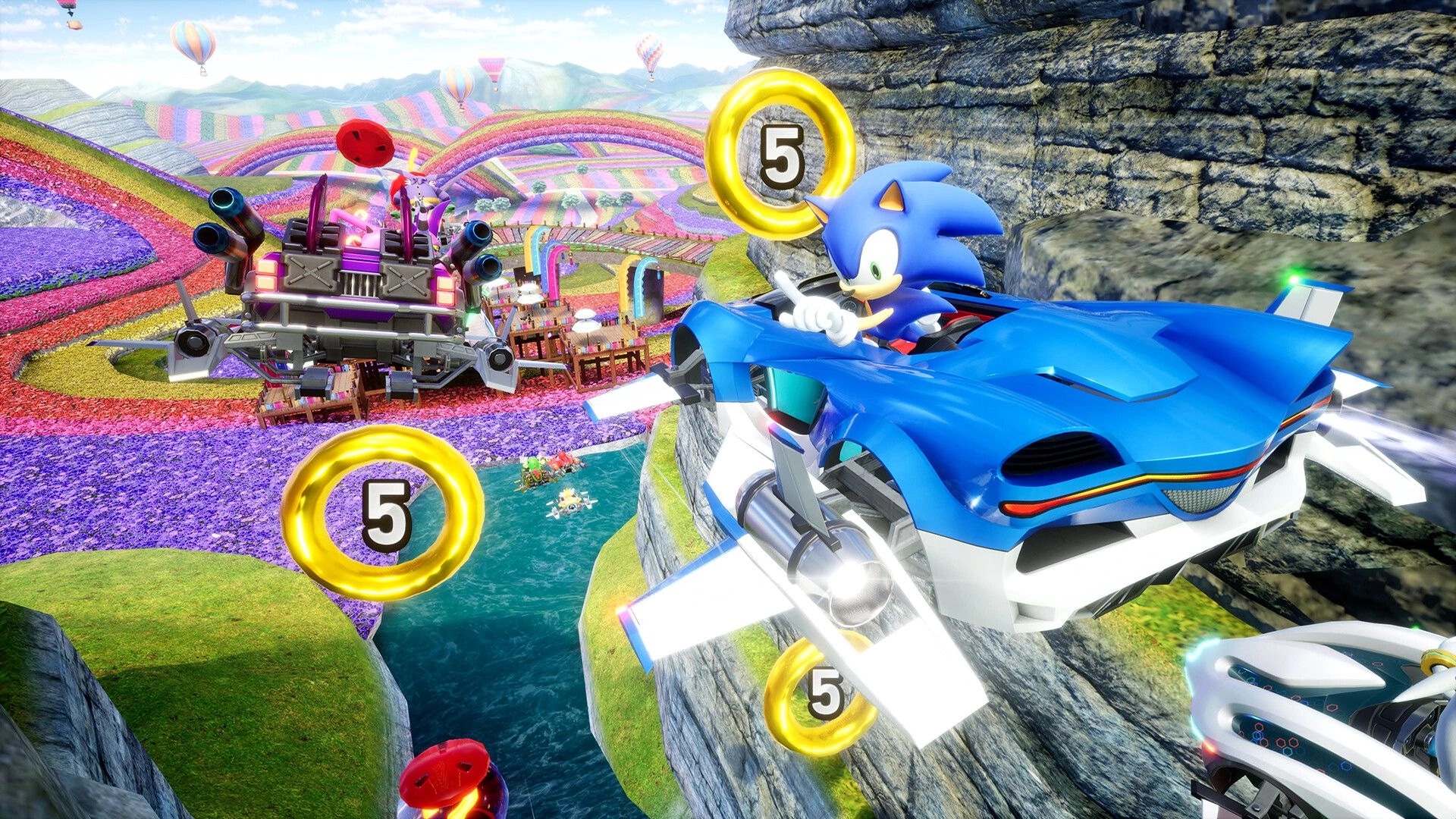 Sonic Racing: Sonic speeds in blue hovercar past rings and rival in vibrant, colorful cliffside track