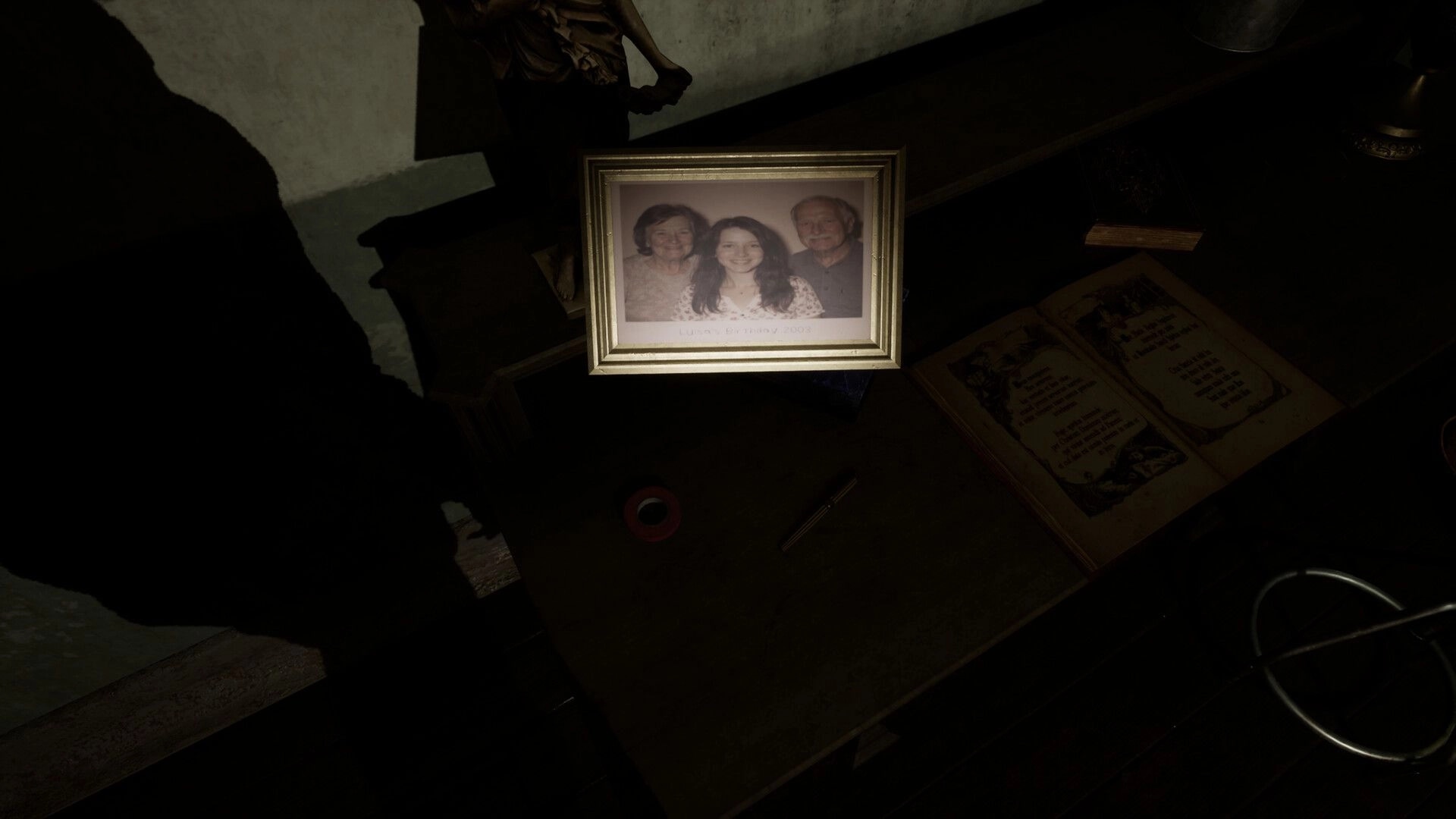 Spiritus Sancti: Flashlight highlights framed family photo and open book on a dusty desk in darkness.