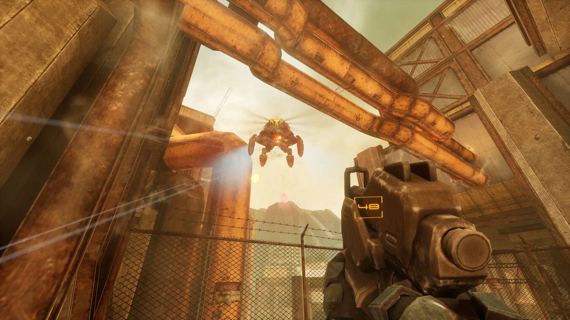 SPRAWL zero: First-person rifle aims at hovering drone amid rusty pipes and fenced industrial yard.