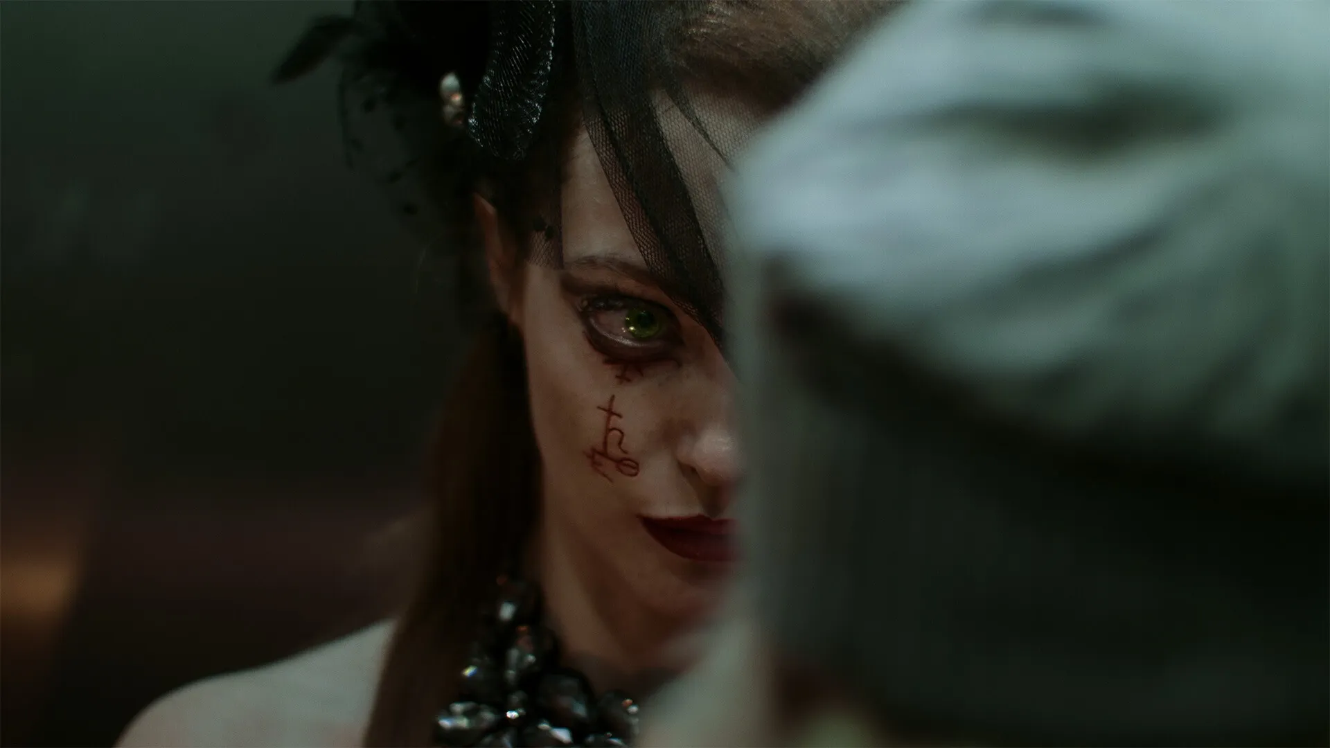 Tenebris Somnia: Close-up of mysterious character with green eye and tattoo in dimly lit environment