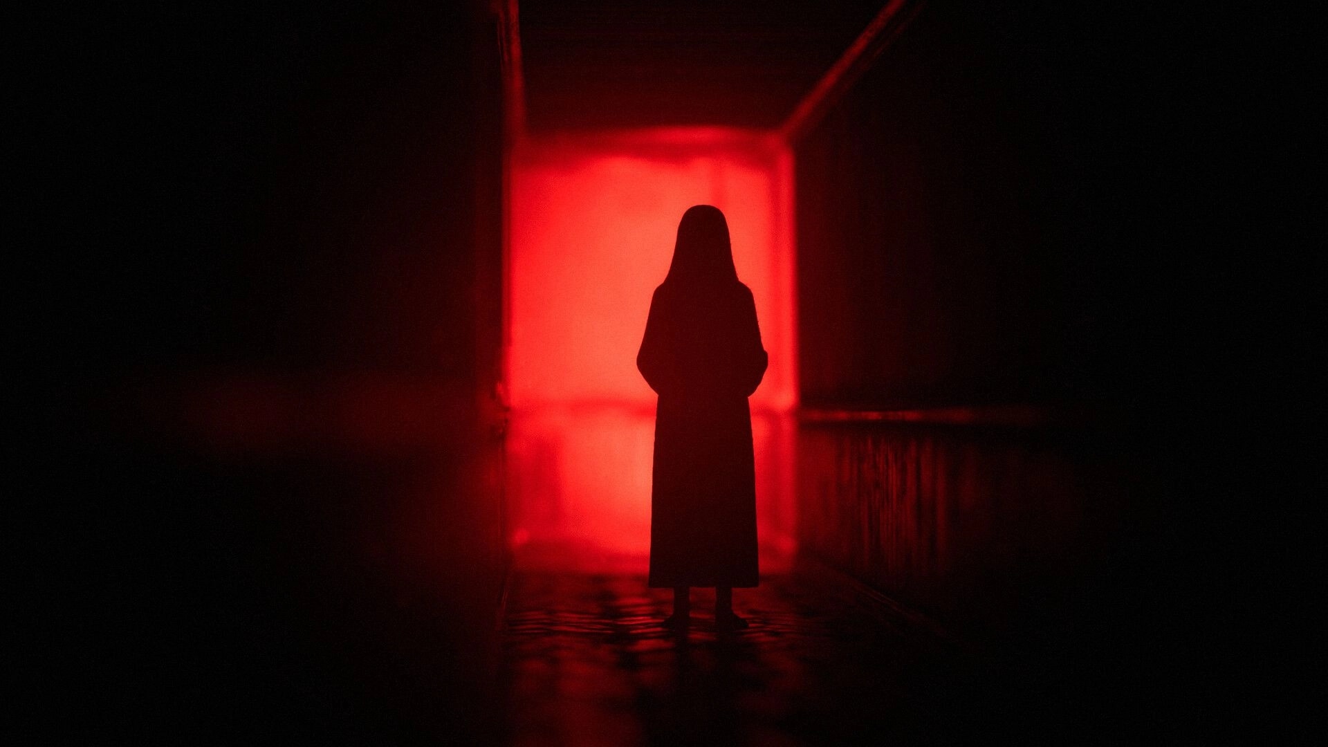 The Unworthy: Hooded figure stands silhouetted in a red-lit corridor with glossy floor reflections.