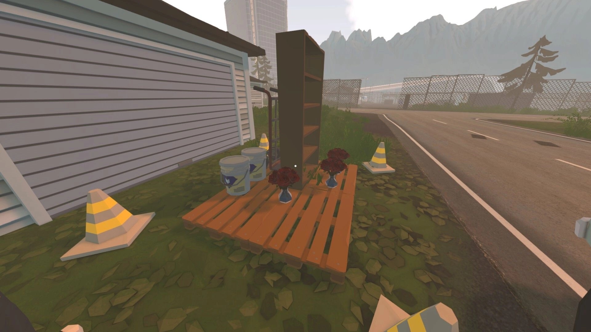Tie Down: First-person view of roadside delivery items on pallets beside a garage and highway fence.