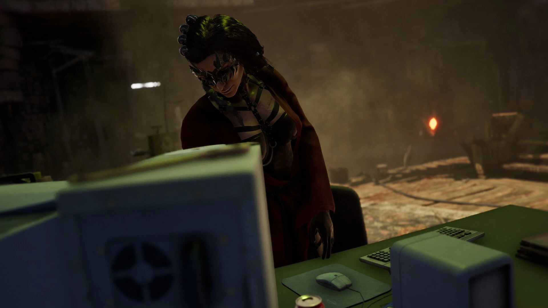 TORMENTOR: Character in dark attire behind a desk with computers in a dimly lit, cluttered room.
