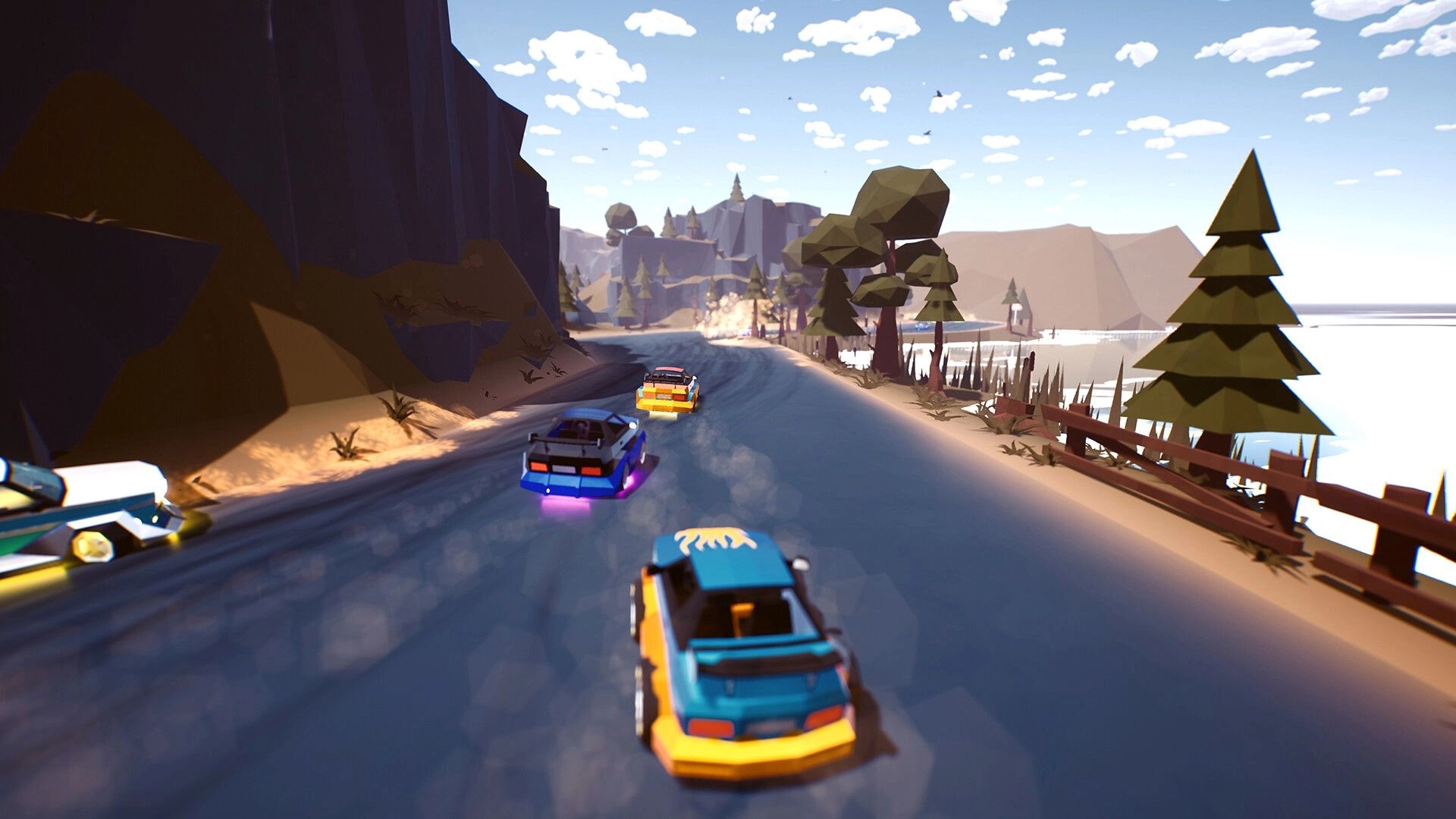 Traks: Three cars drift along a curving mountain road beside a lake with trees and fences.