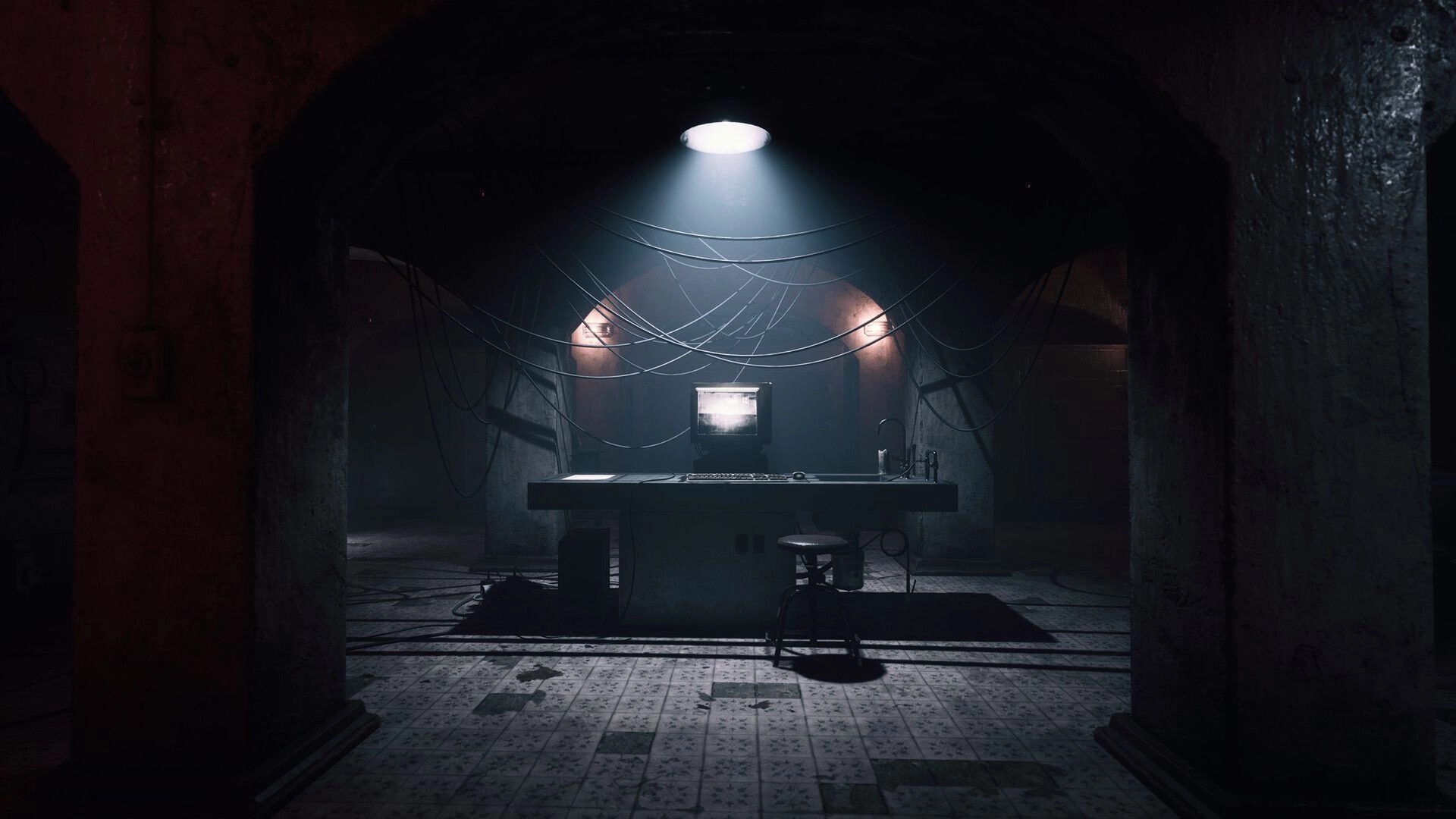 UNHOST: Surveillance monitor on a desk under hanging cables in a dim, tiled underground room.